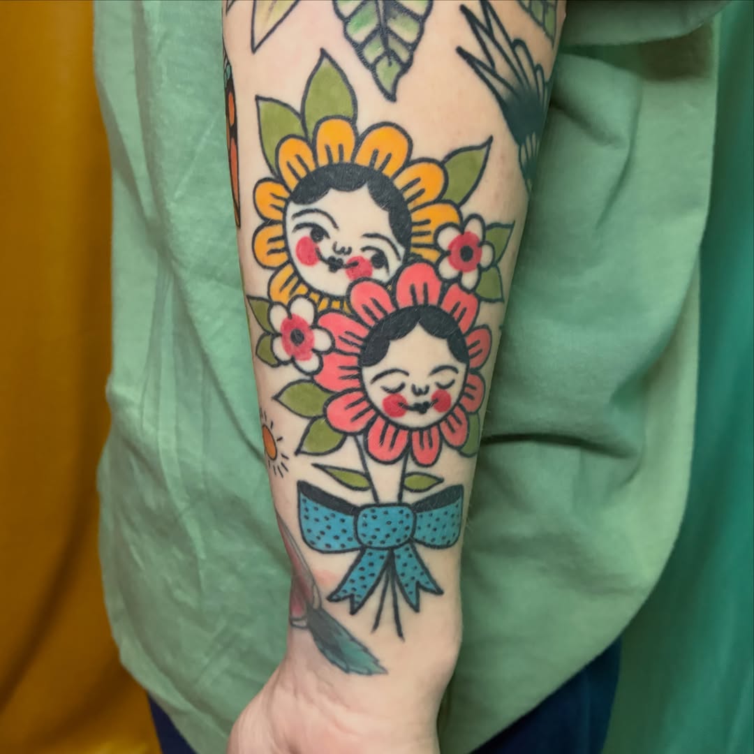 Doll faces in flowers American traditional tattoo on the forearm by Kaily McKee