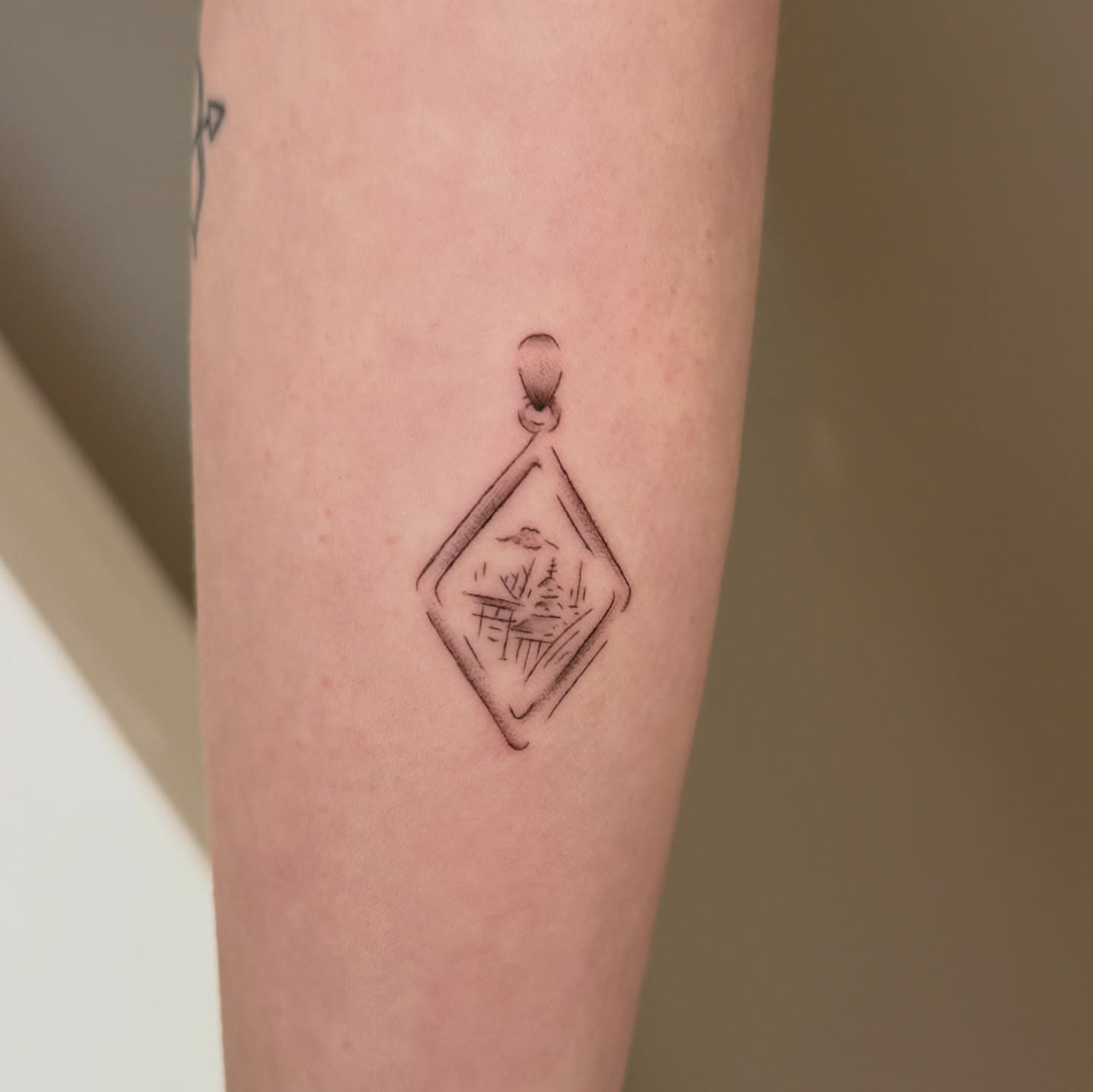 Pendant with landscape geometric tattoo on the forearm by Fine Line Tattoos