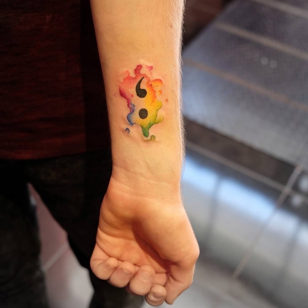 Semicolon with watercolor splash watercolor tattoo on the forearm by Yana Aizen
