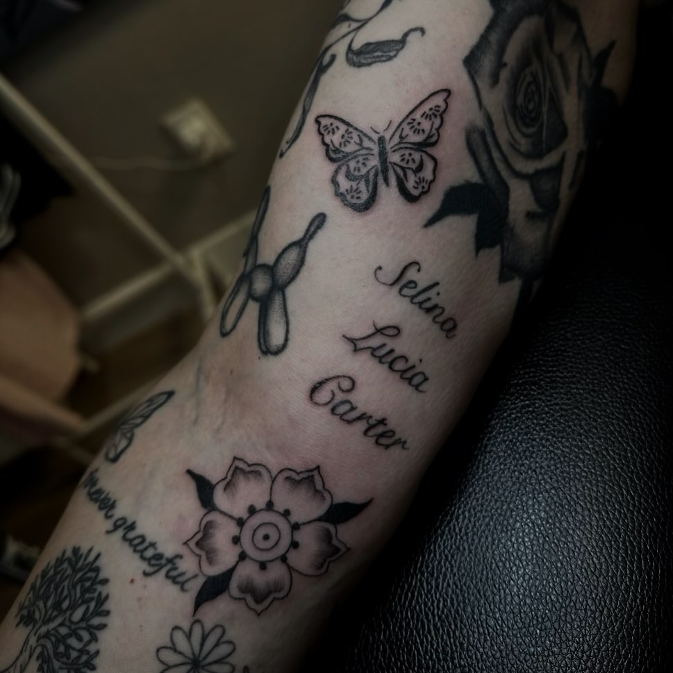 Flower, butterfly, names black and grey tattoo on the forearm by Marly Quinn