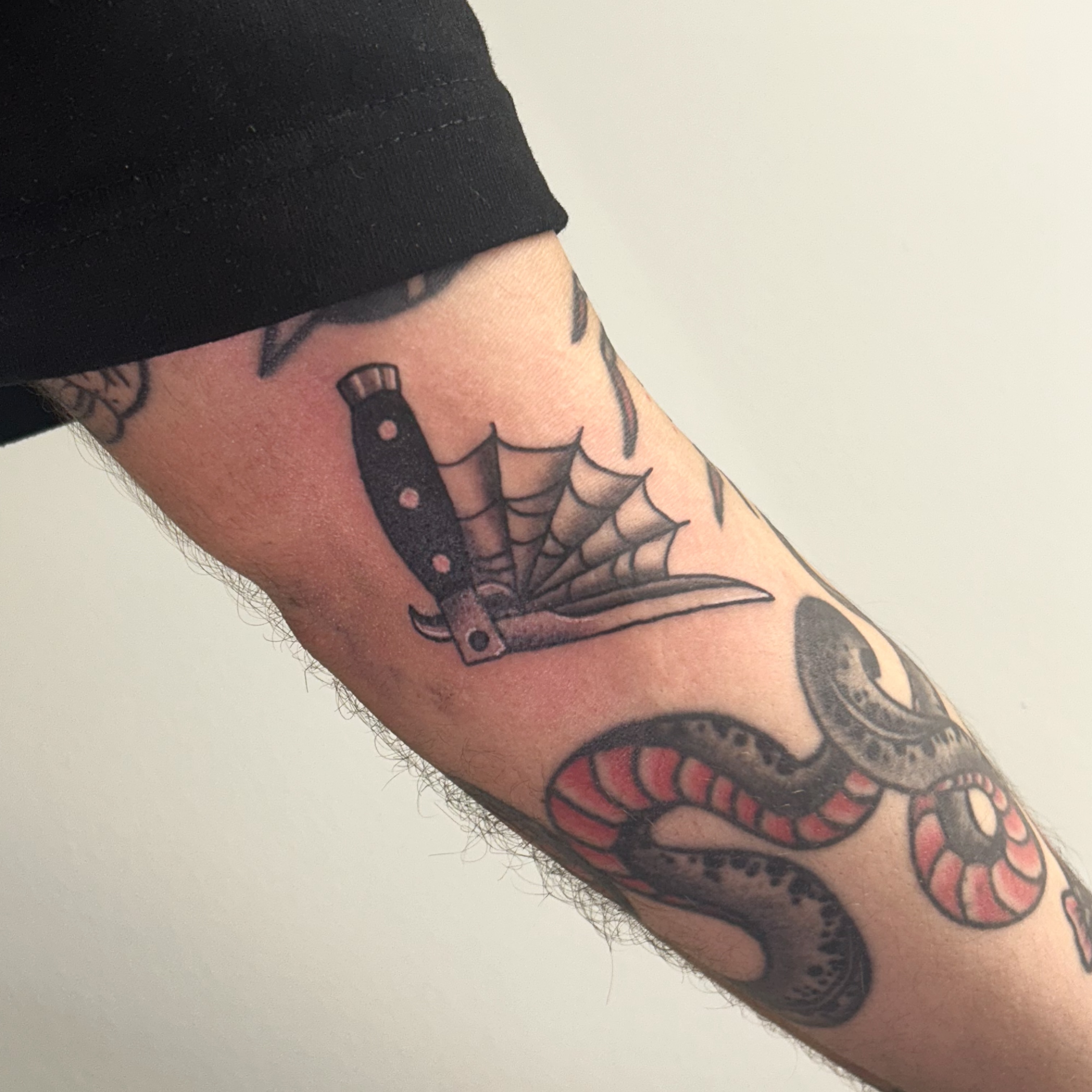 Knife and spiderweb American traditional tattoo on the forearm by Tawni Bender