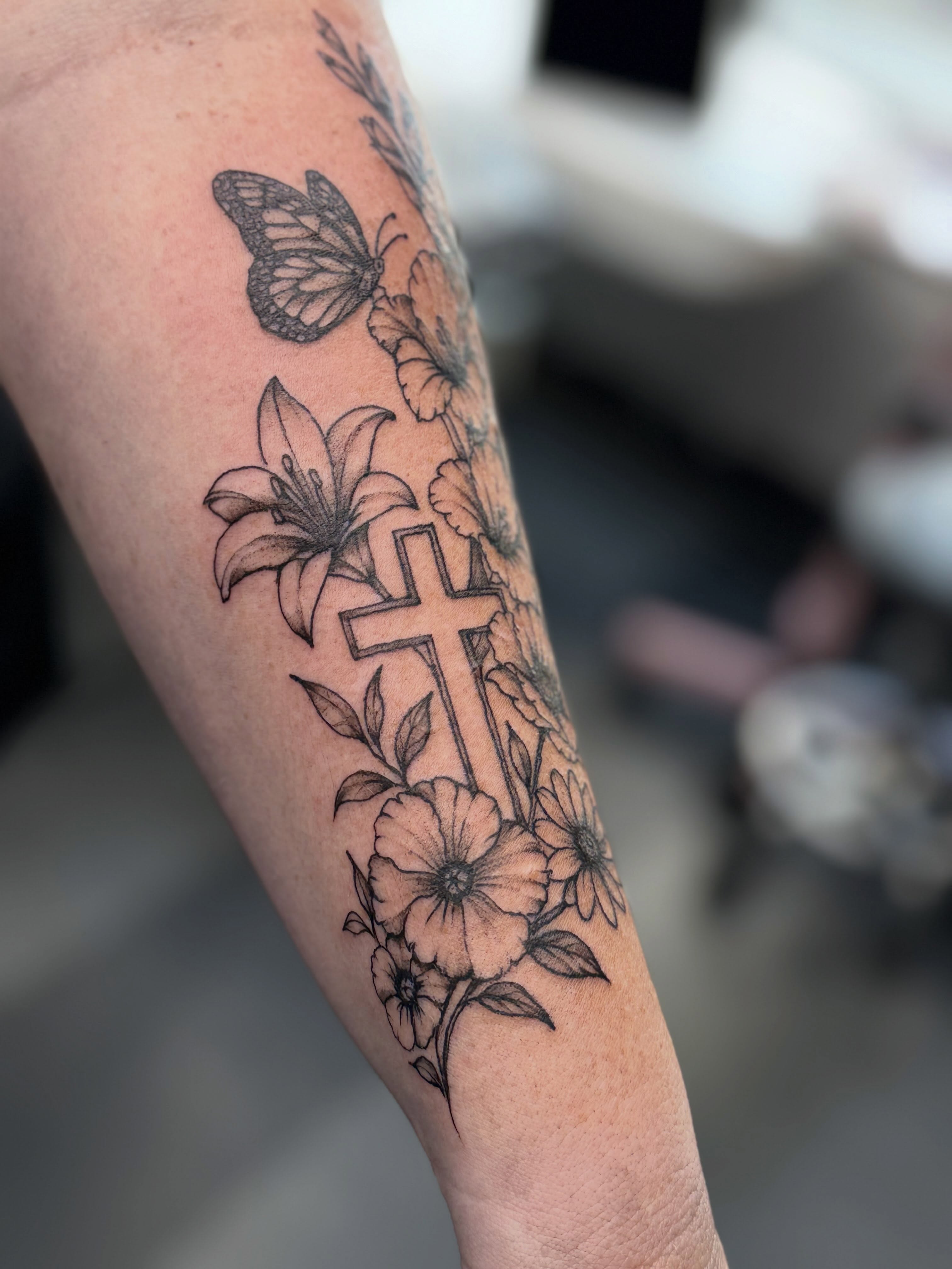 Cross and flowers black and grey tattoo on the forearm by Tetiana