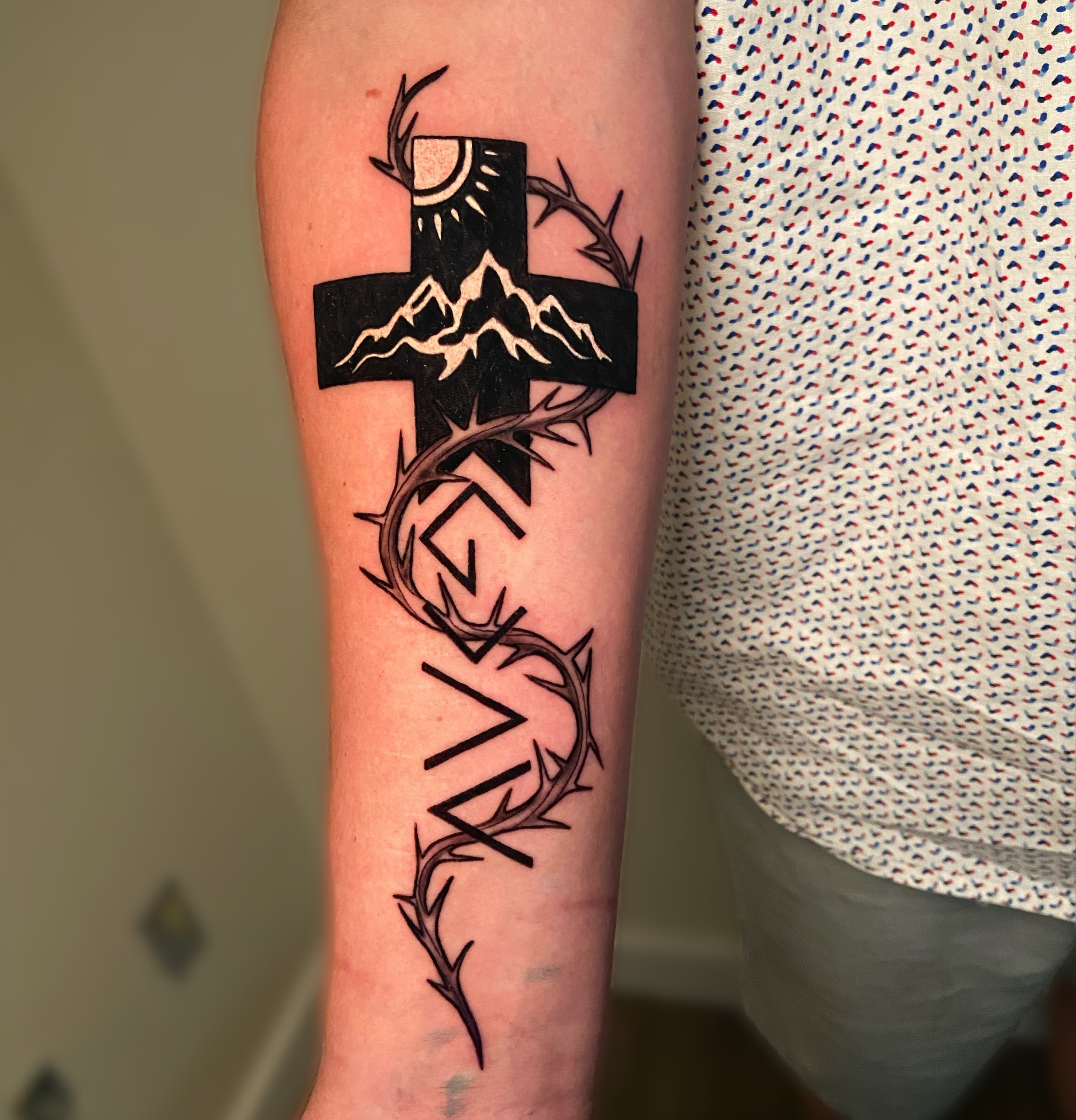 Cross with crown of thorns black and grey tattoo on the forearm by Ezra Gonda
