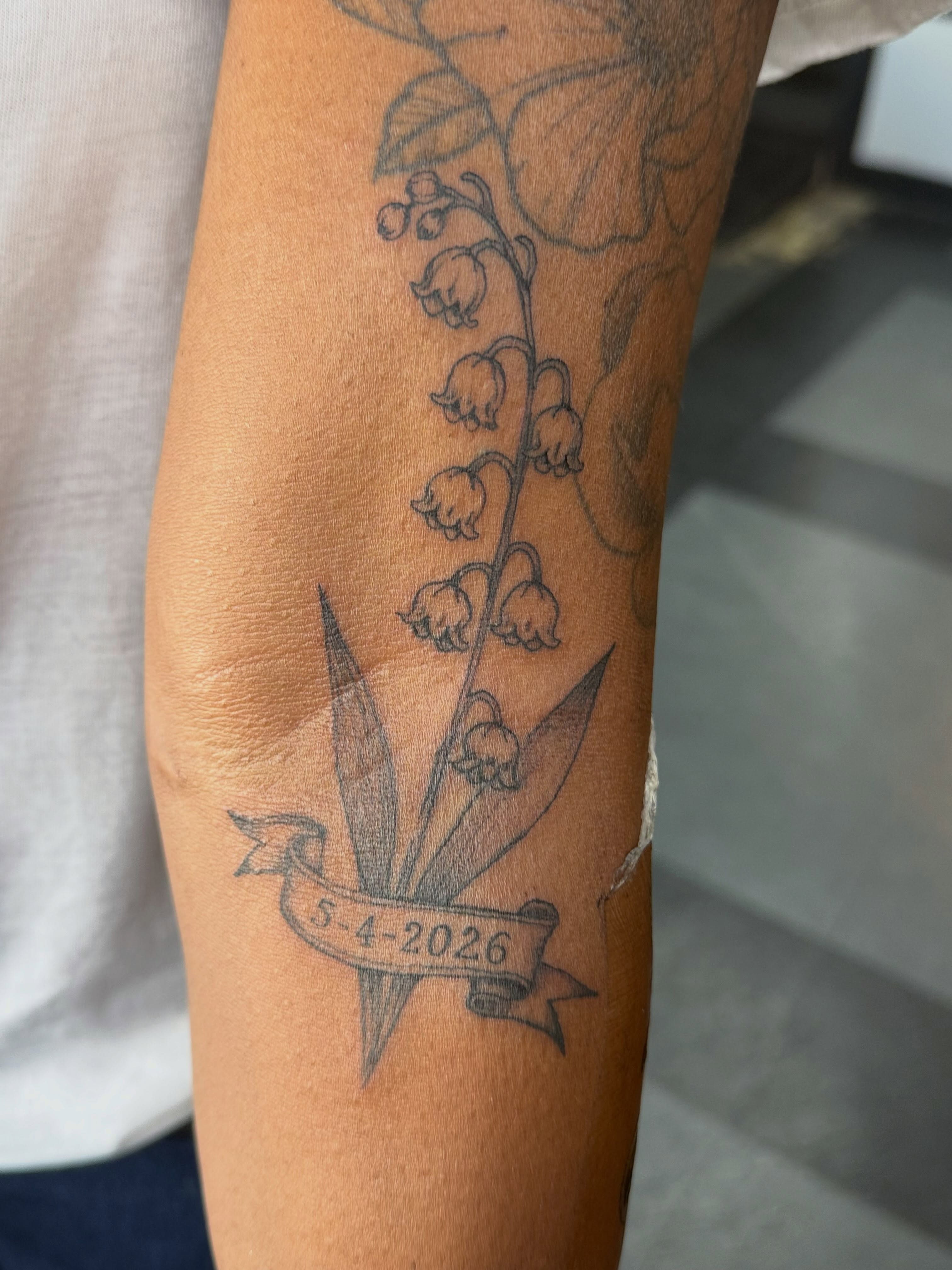 Lily of the valley black and grey tattoo on the forearm by Tetiana