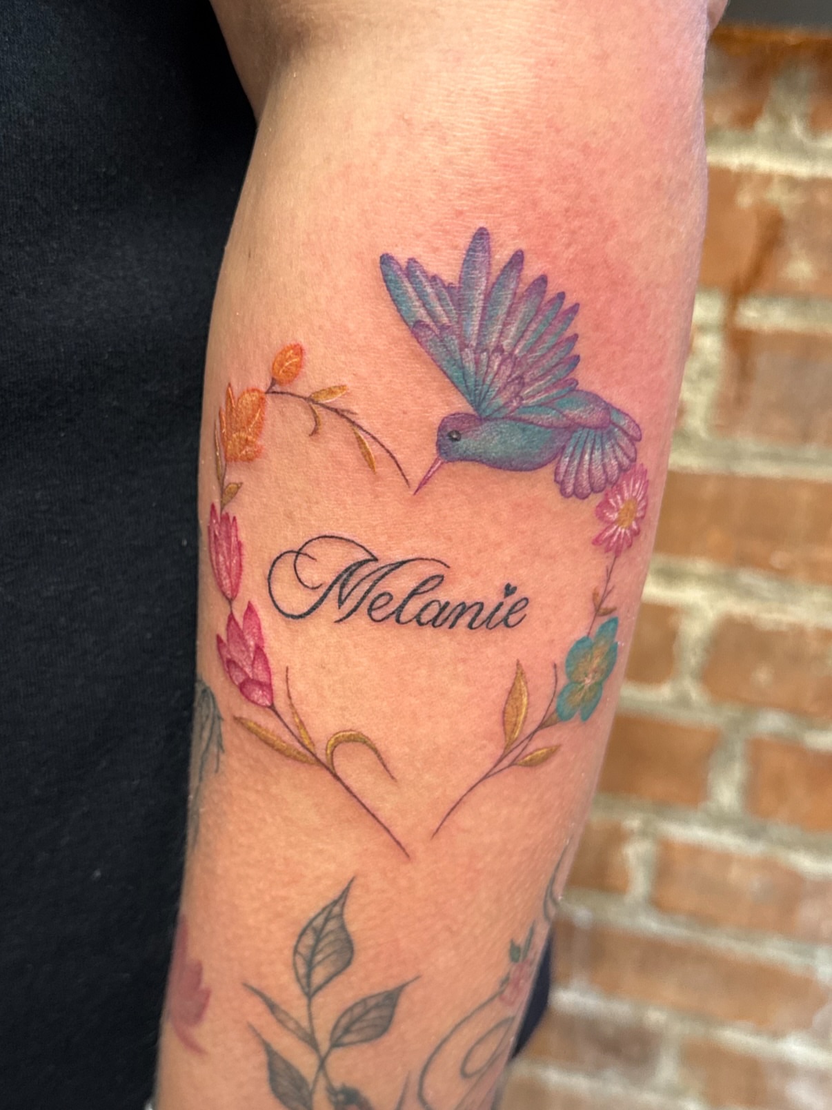 Hummingbird and floral wreath new school tattoo on the forearm by Royal Martinez