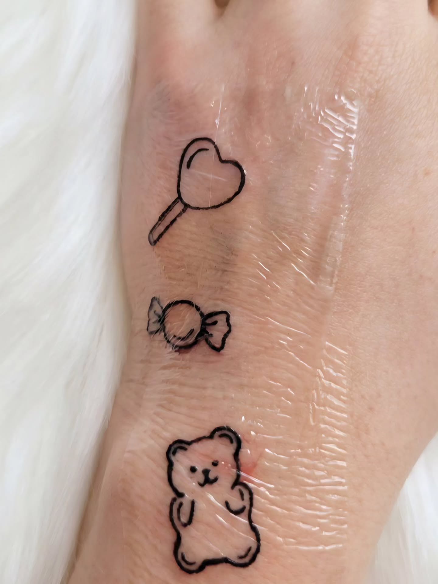 Heart, candy, teddy bear minimalist tattoo on the forearm by Peach & Poke, Lethbridge, Alberta