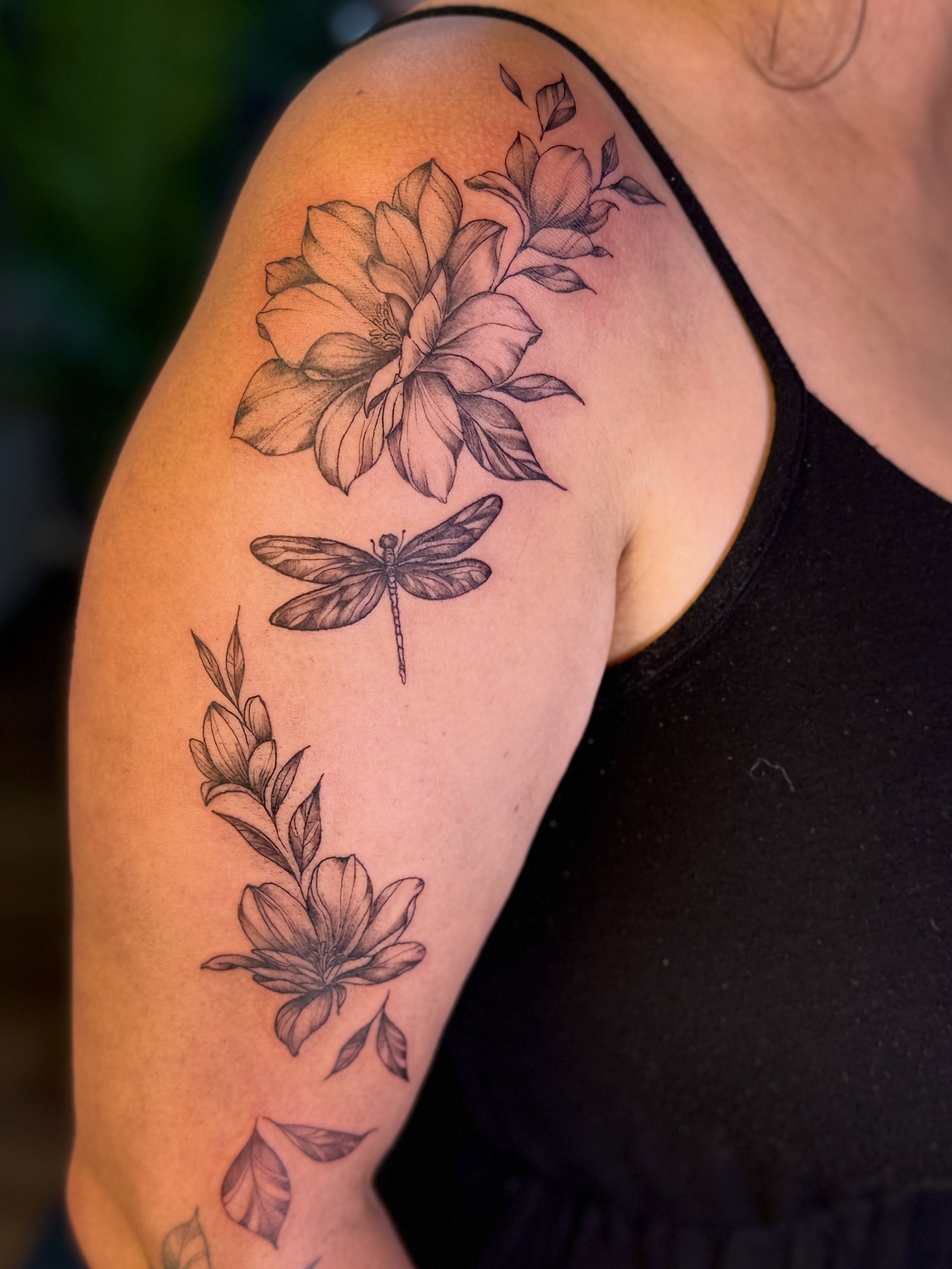 Flower and dragonfly black and grey tattoo on the upper arm by Tetiana