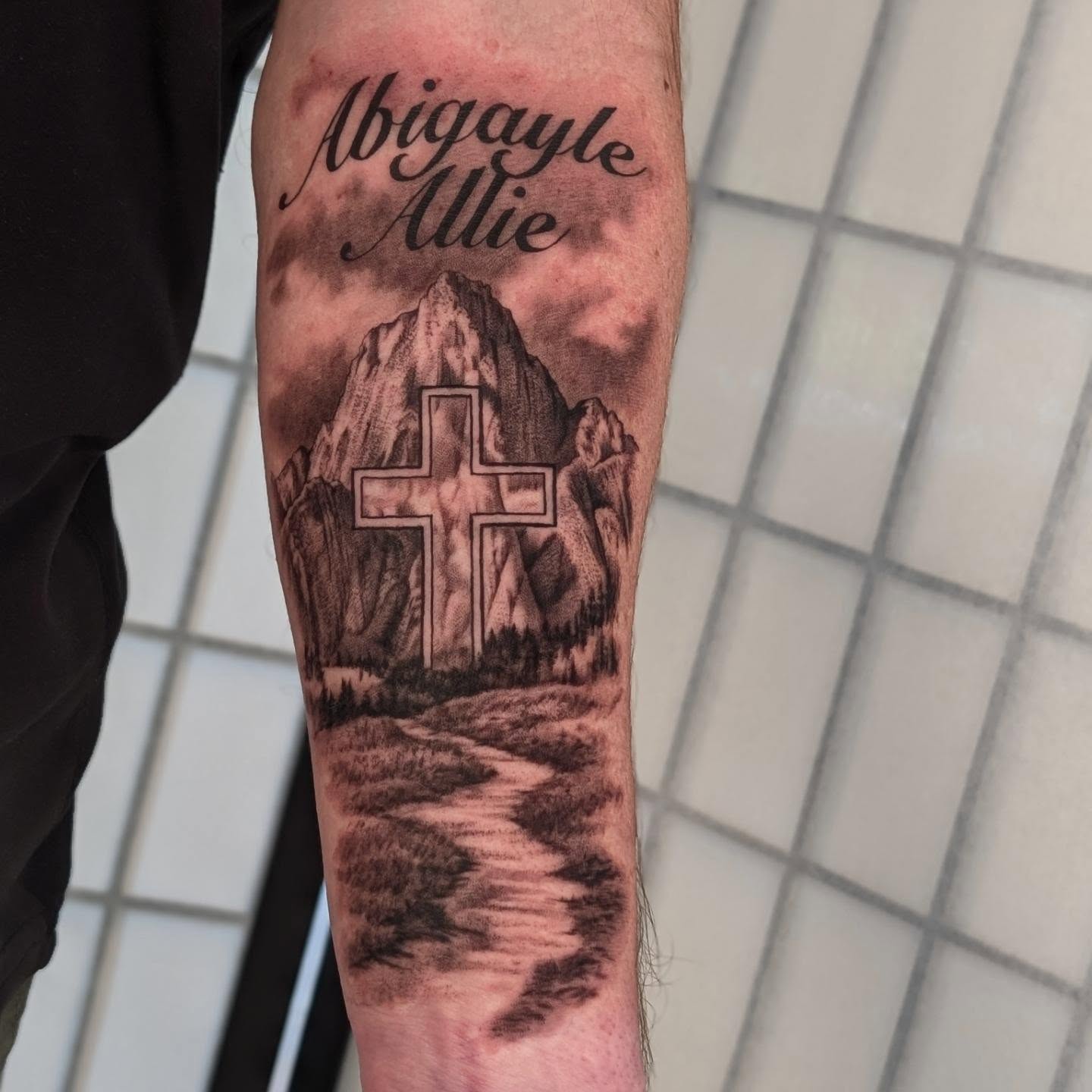 Mountain landscape with cross realism tattoo on the forearm by Sean Costello