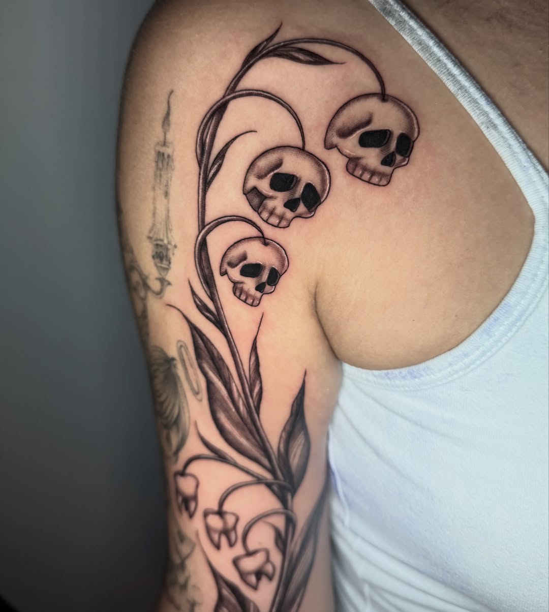 Skulls and lilies of the valley black and grey tattoo on the upper arm by 𝖎𝖘𝖆 ✶ 𝖉𝖋𝖜 𝖙𝖆𝖙𝖙𝖔𝖔𝖘