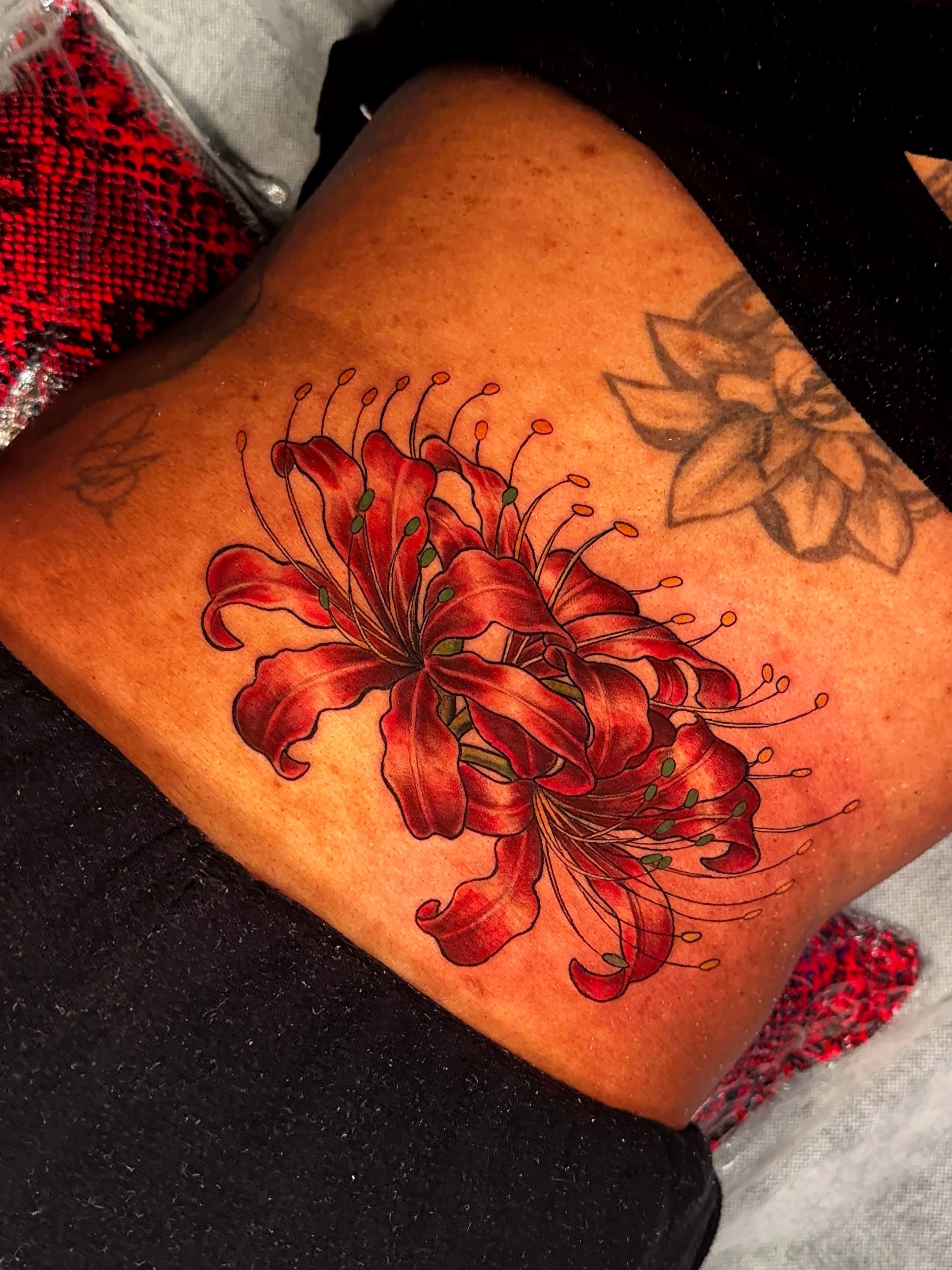 Red lilies realism tattoo on the thigh by Ericka Hampton, Ferndale, Michigan