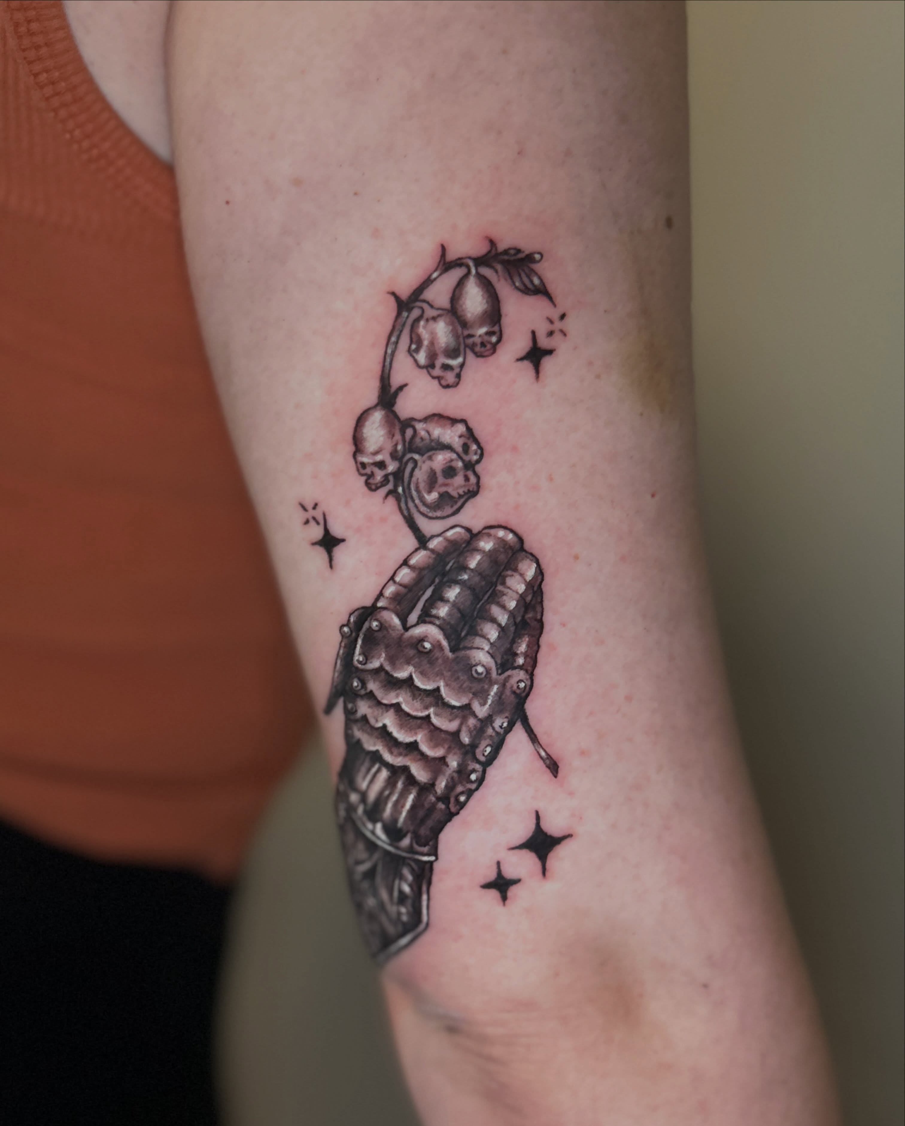 Praying hand with skulls and lilies black and grey tattoo on the forearm by Alex