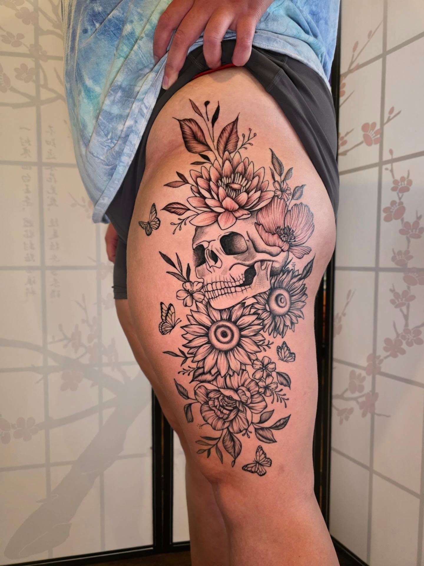 Skull and flowers black and grey tattoo on the thigh by Maggie