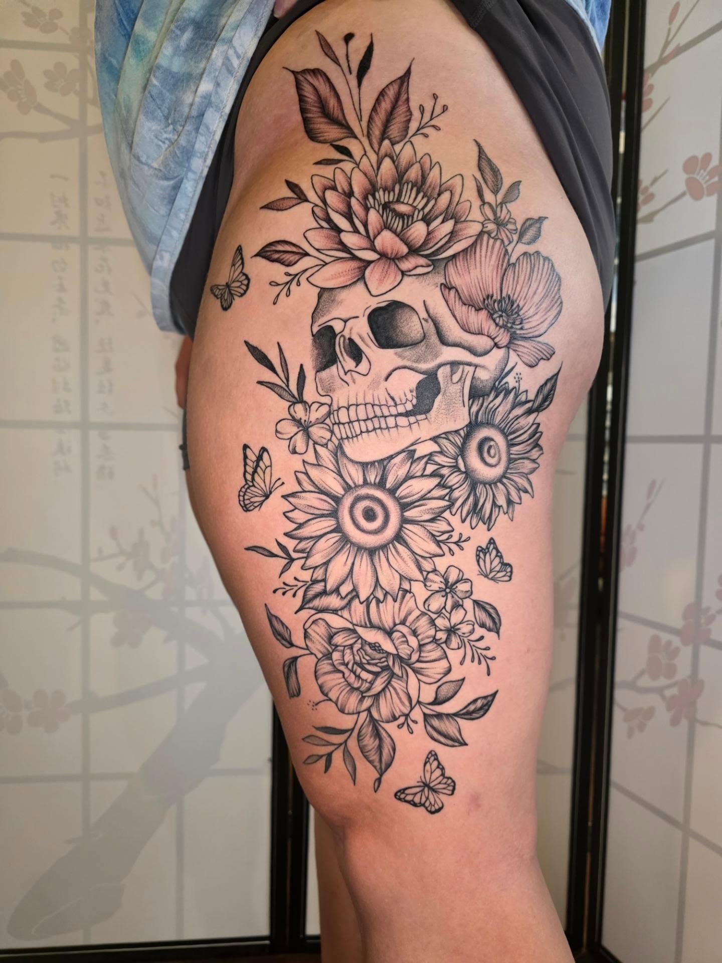 Skull and flowers black and grey tattoo on the thigh by Maggie