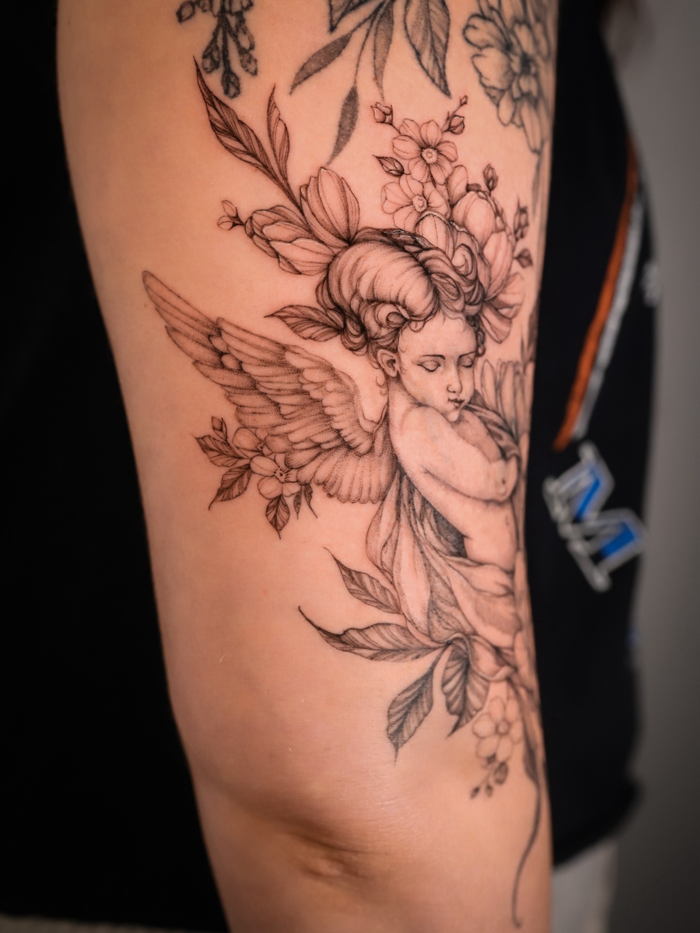 Cherub with flowers realism tattoo on the forearm by Caroline + Utah Tattoo Artist
