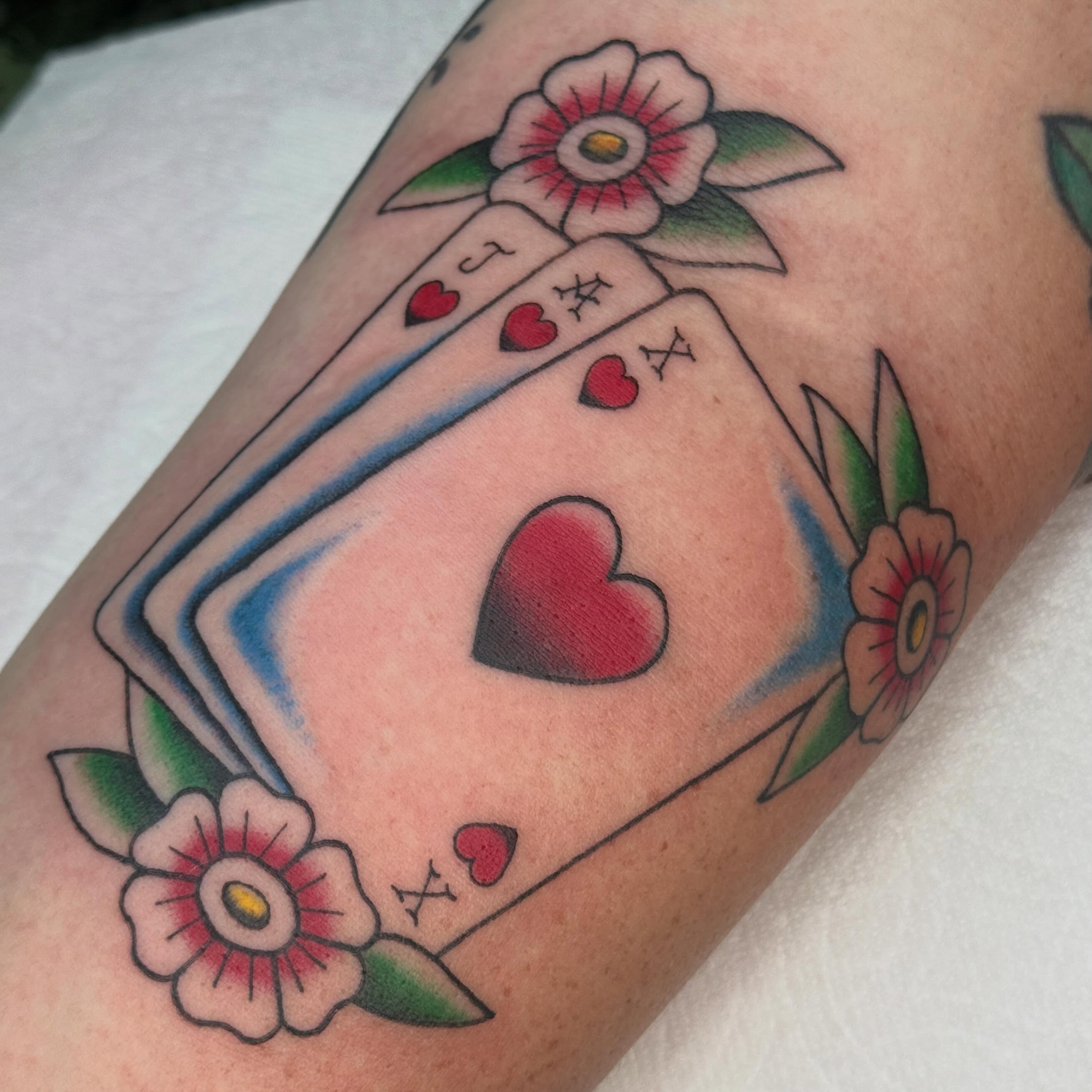 Playing cards and flowers American traditional tattoo on the forearm by chloe jeanel estrada