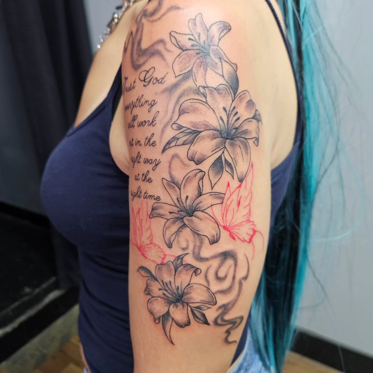 Lilies and inspirational quote black and grey tattoo on the upper arm by Danny