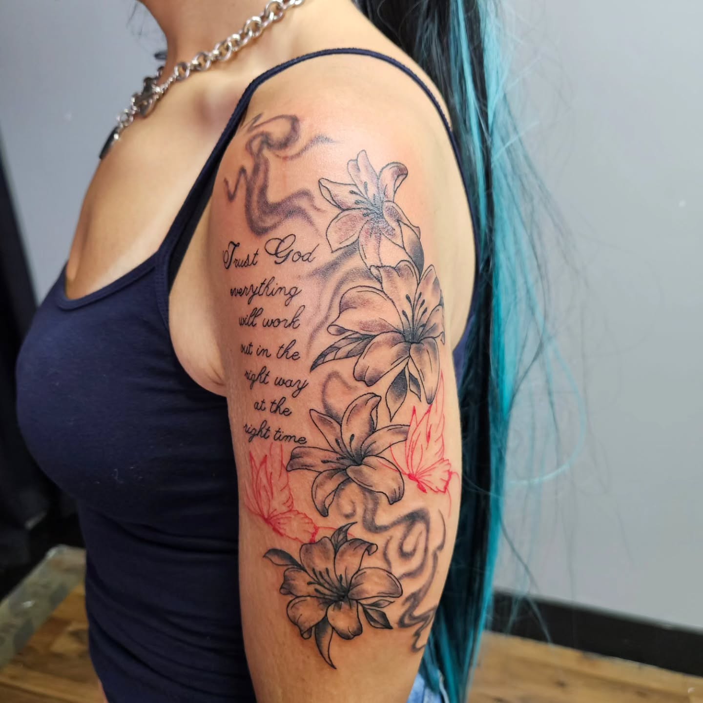 Flowers and inspirational quote black and grey tattoo on the upper arm by Danny