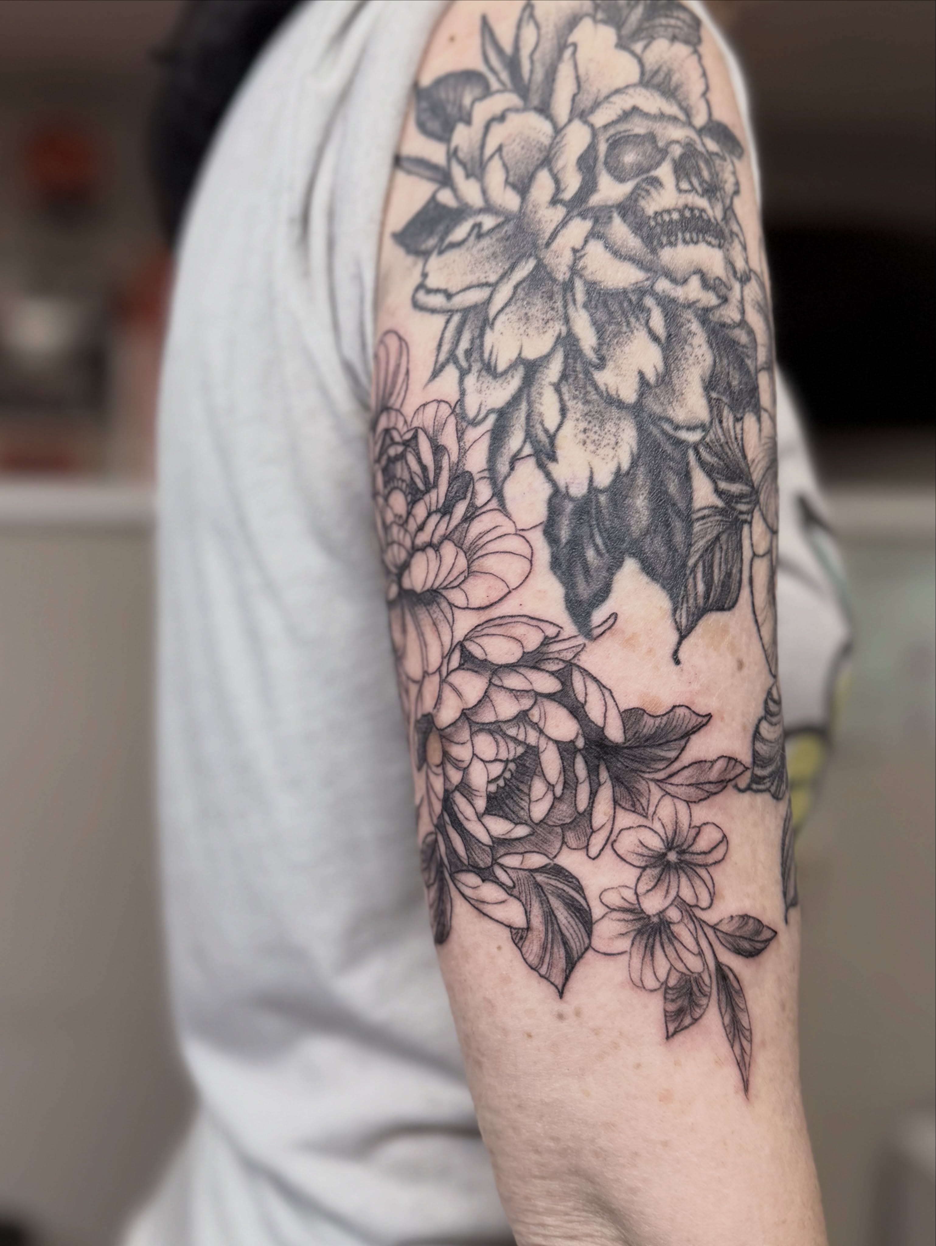 Floral arrangement with skull realism tattoo on the forearm by Skylar Sheeley