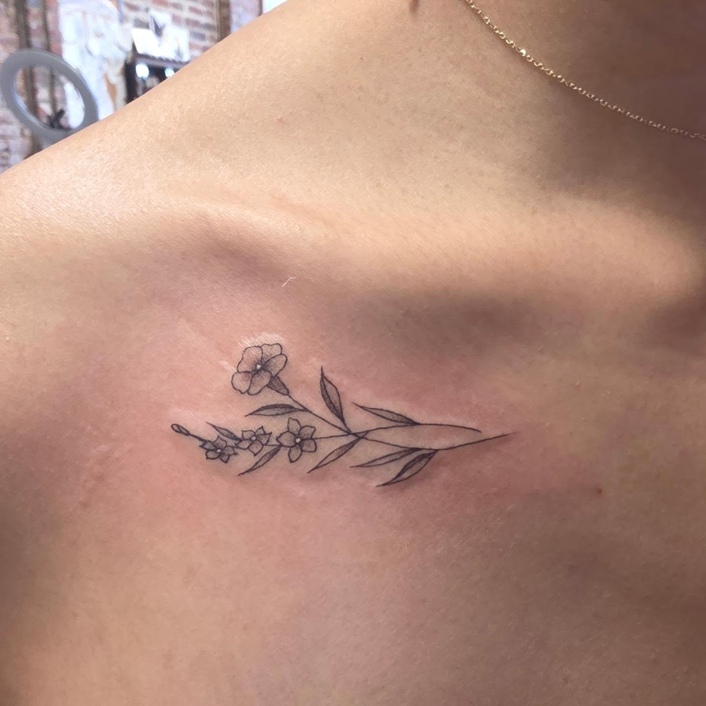 Floral branch fine line tattoo on the chest by Tattoos by Annie