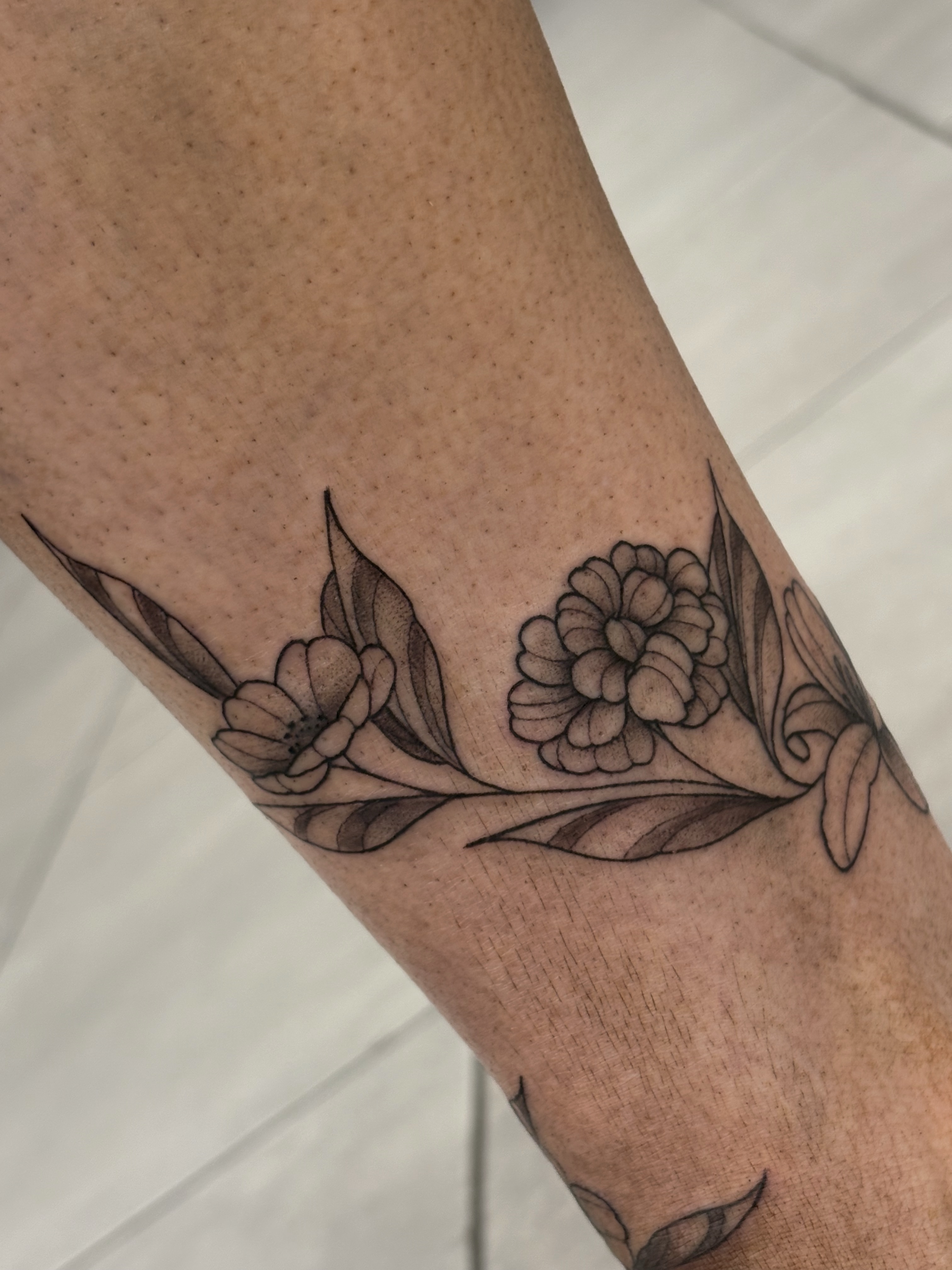 Floral arrangement black and grey tattoo on the forearm by Fine Line Tattoo Artist