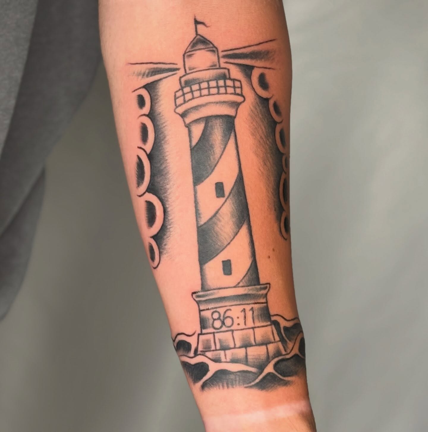 Lighthouse black and grey tattoo on the forearm by Elmer Lethco