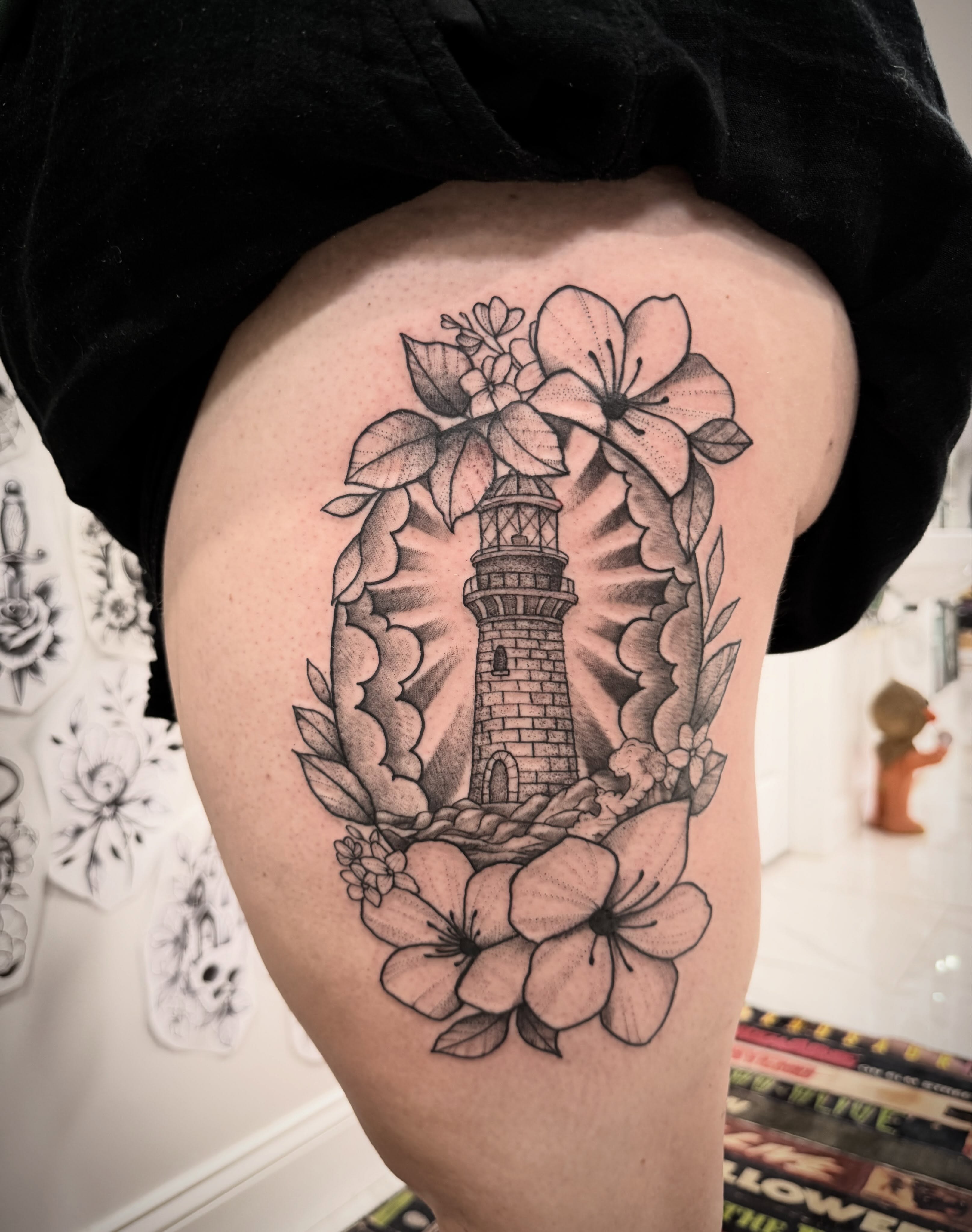Lighthouse and flowers black and grey tattoo on the thigh by Shannon Misitano