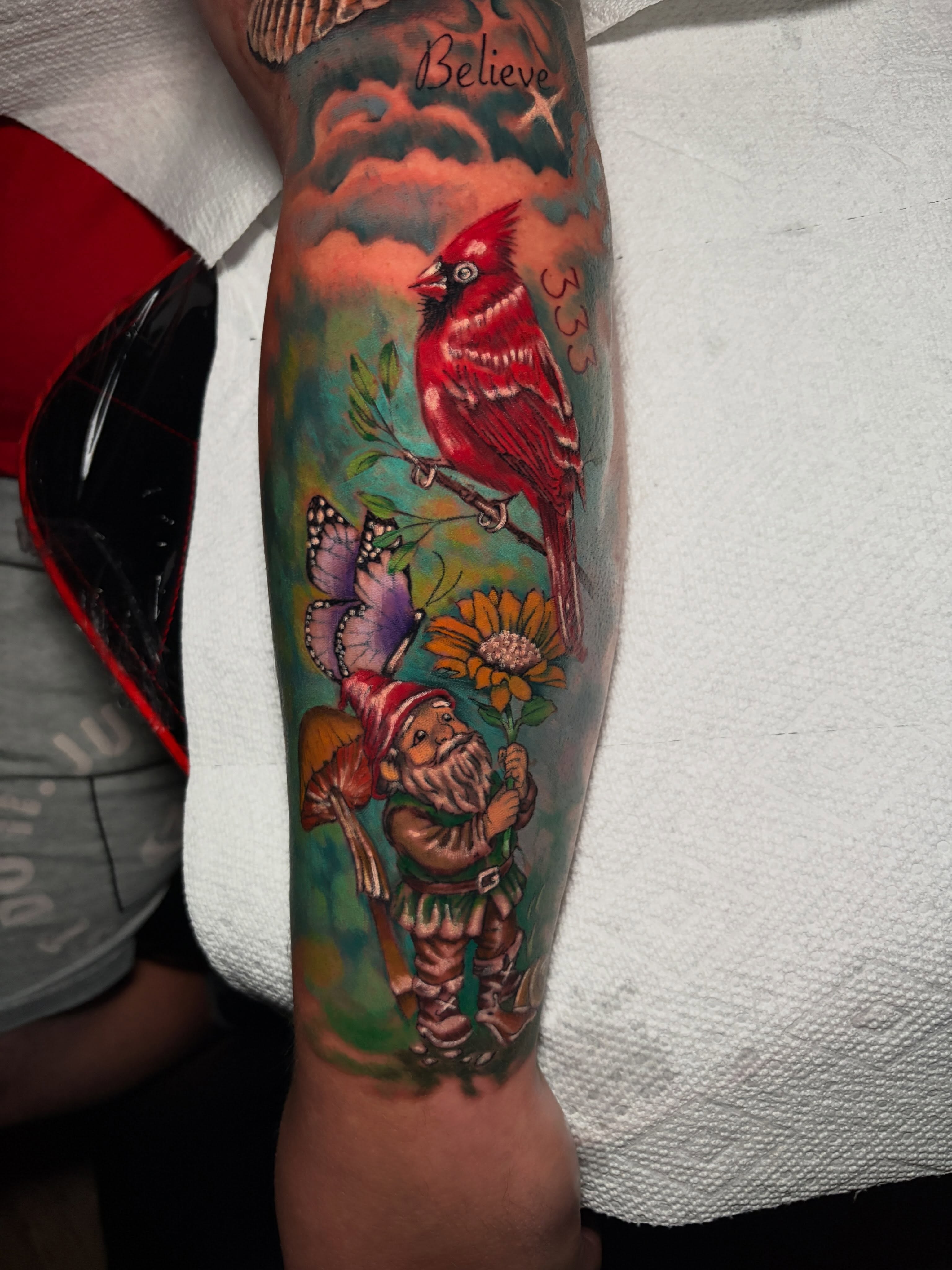 Red cardinal and gnome realism tattoo on the forearm by Ashley Denise