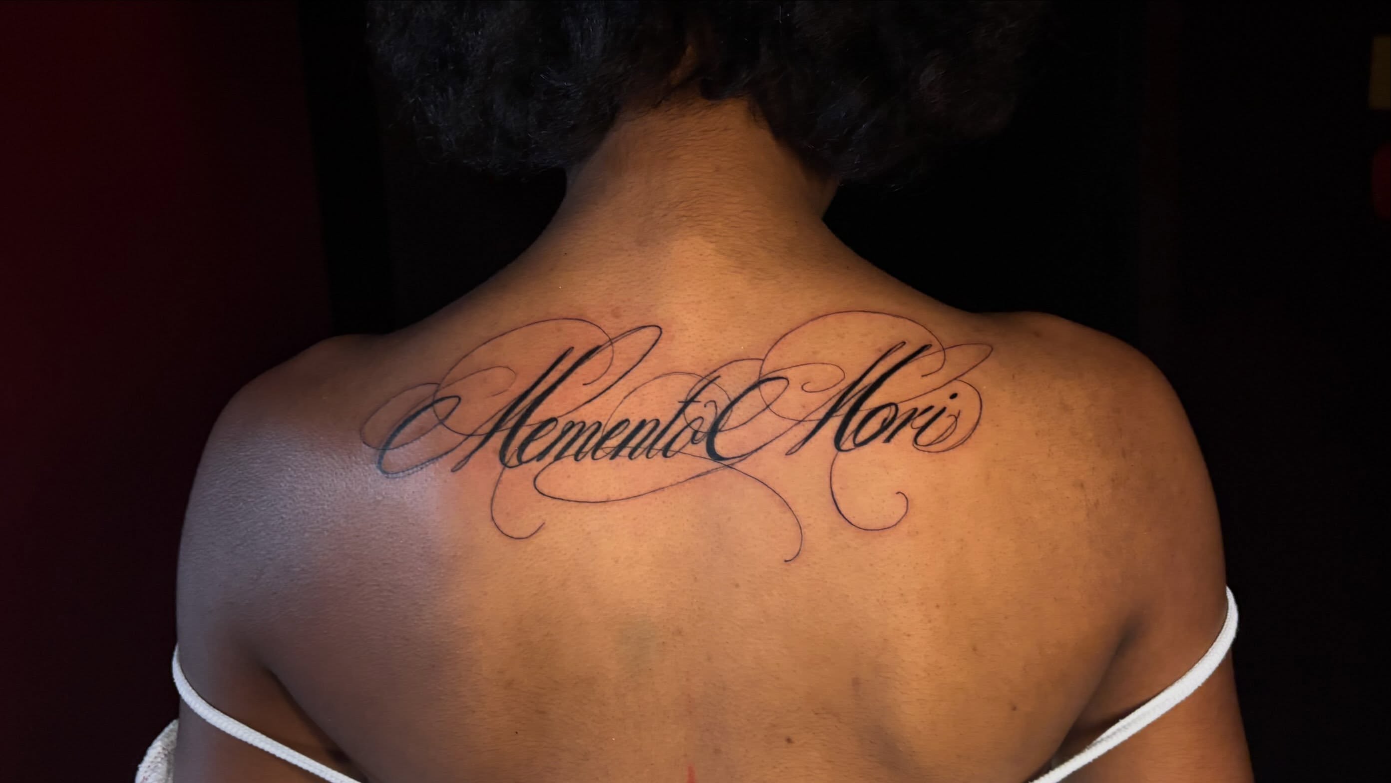 Memento Mori lettering script tattoo on the back by Kells