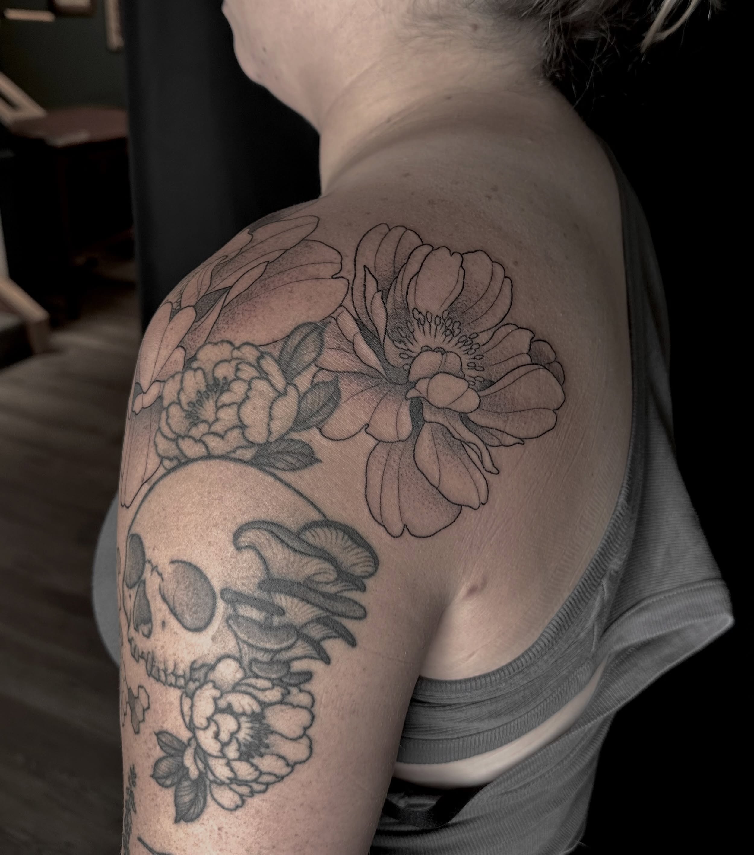 Skull and flowers black and grey tattoo on the shoulder by Zoe Arrigo