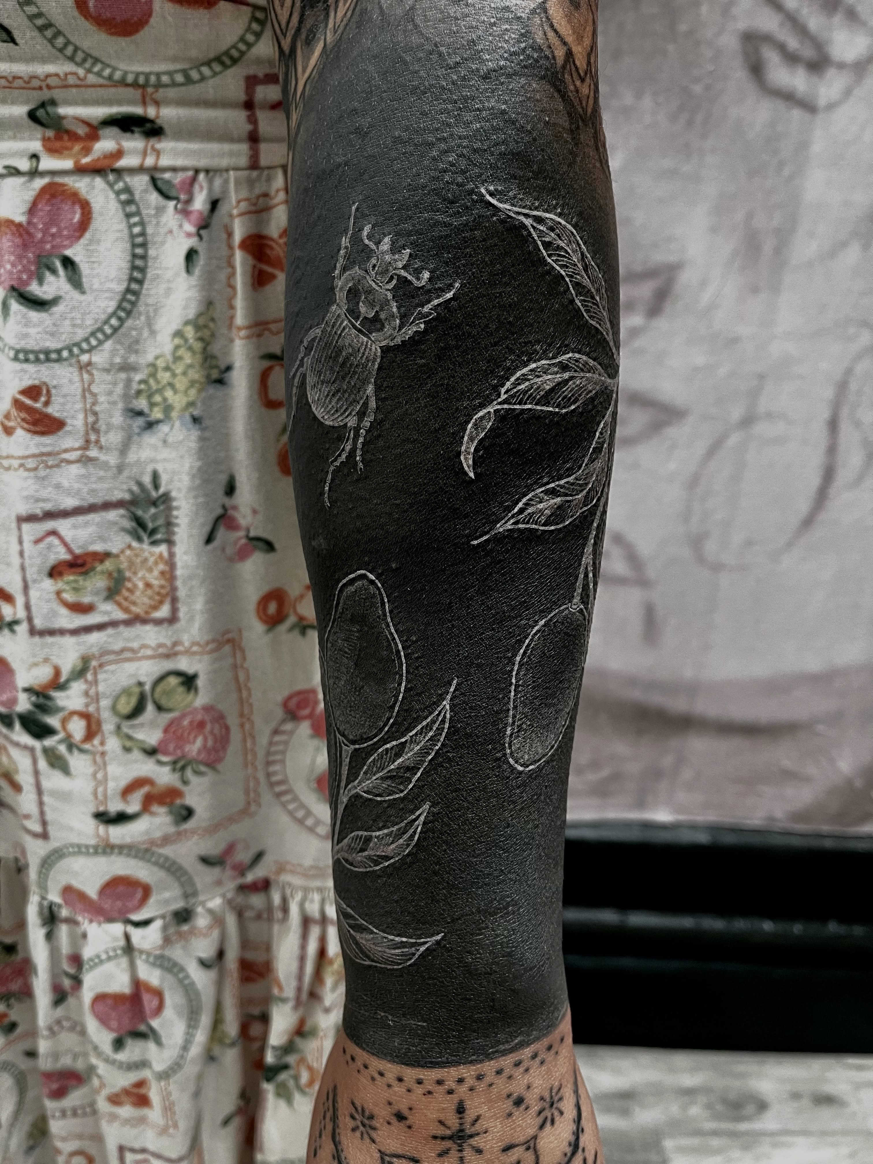 Scarab beetle and fruit black and grey tattoo on the forearm by Lo Gwynn