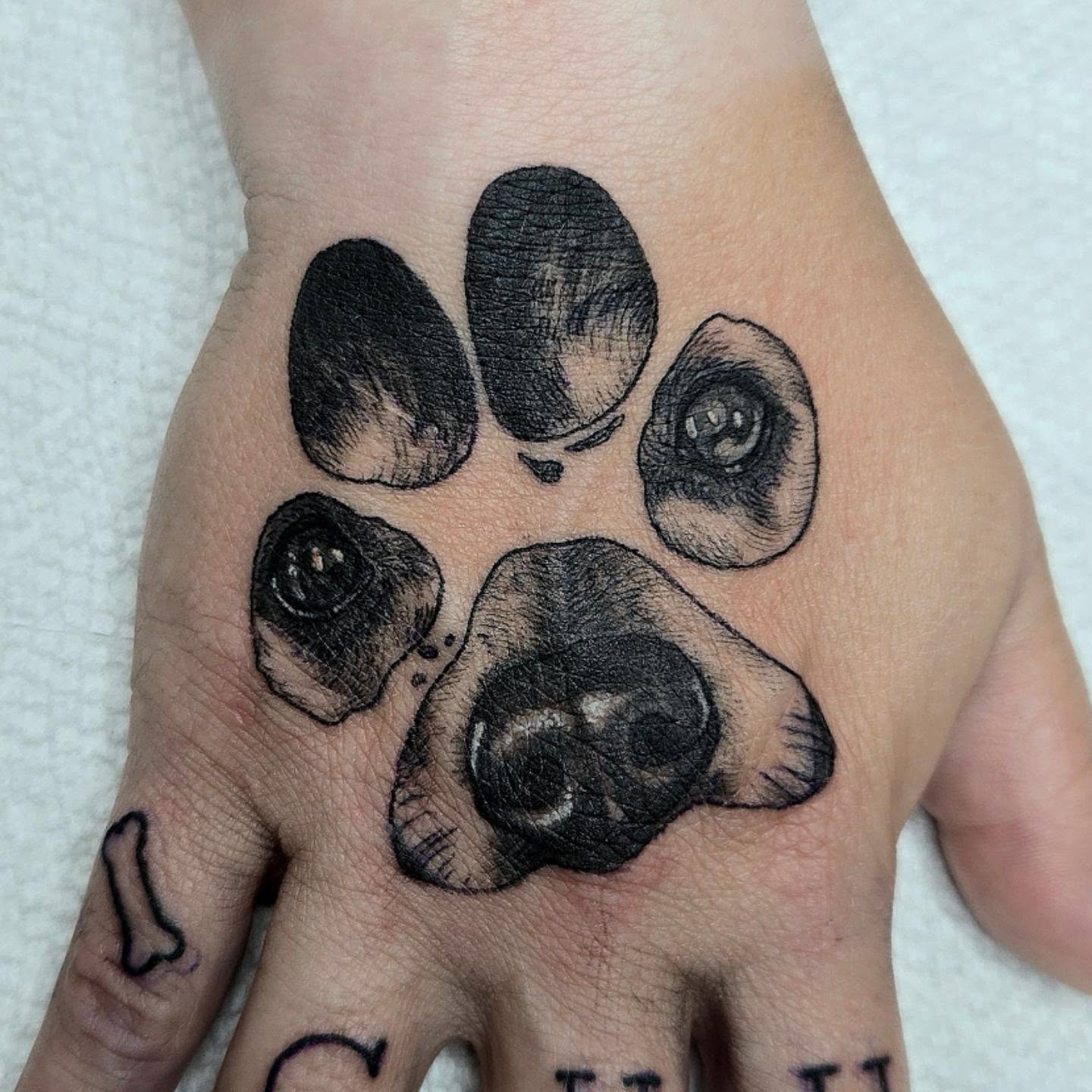Dog paw black and grey tattoo on the hand by Amanda Hinrichs