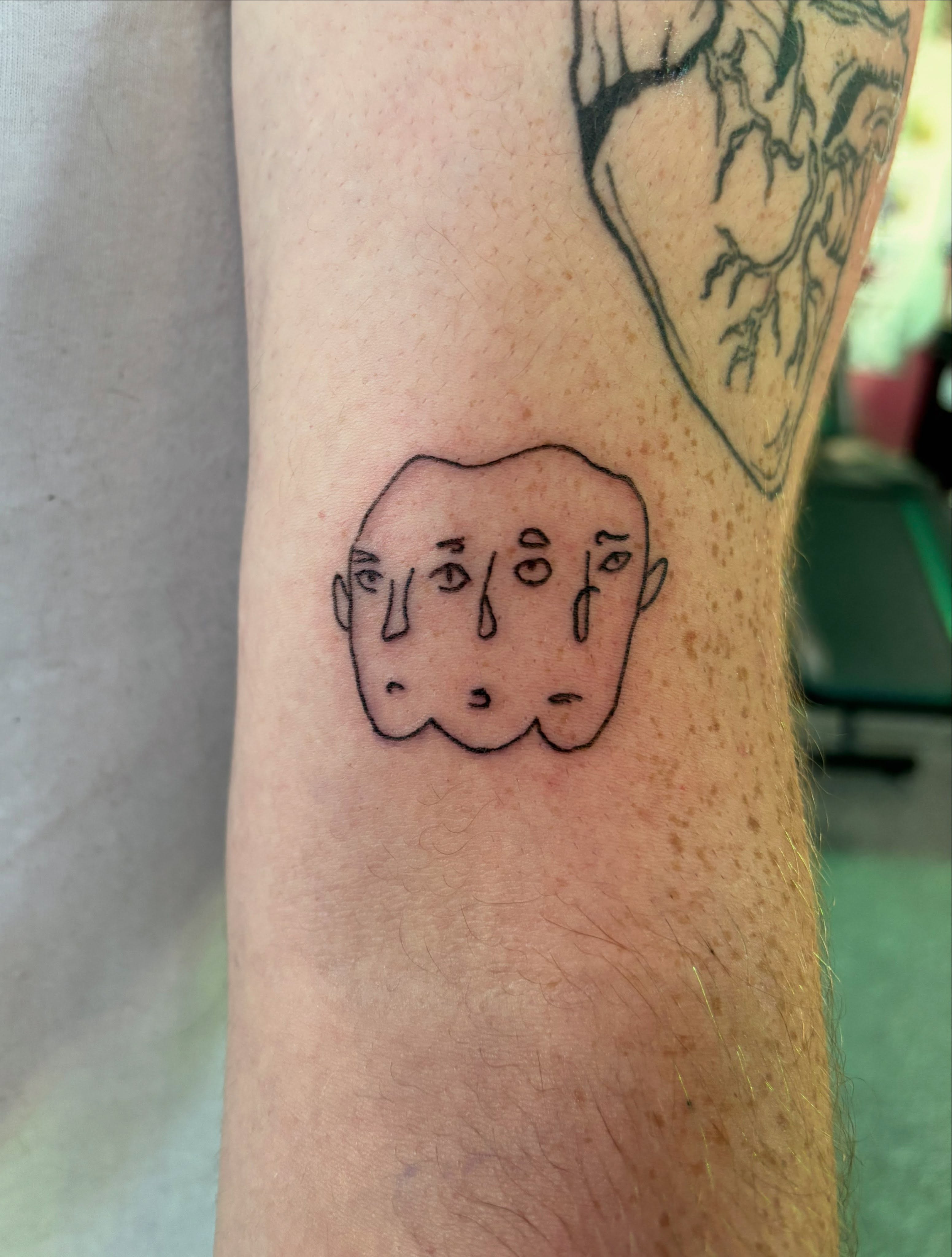 Abstract face minimalist tattoo on the forearm by Hiro Robinson