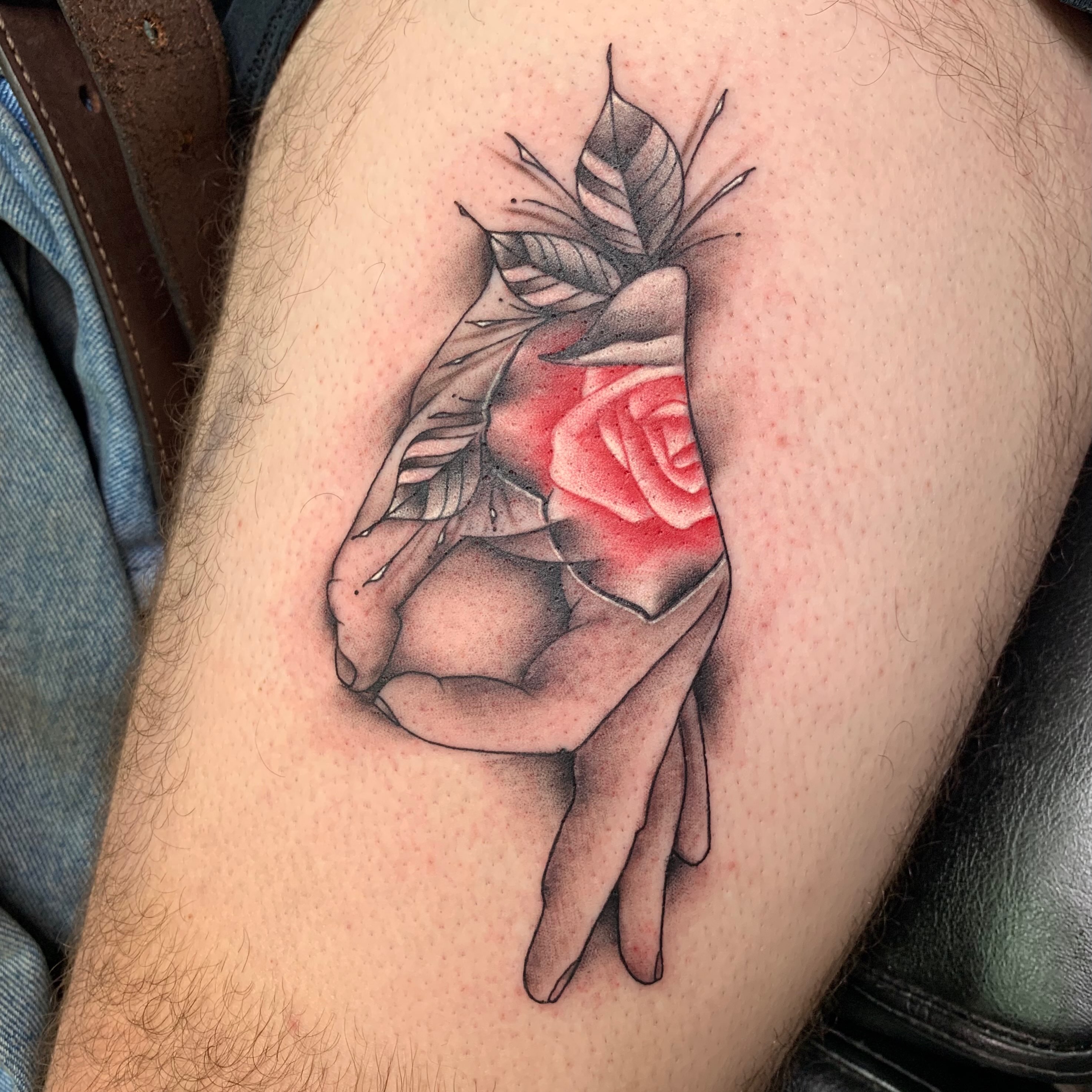 Hand holding rose realism tattoo on the thigh by Cuda
