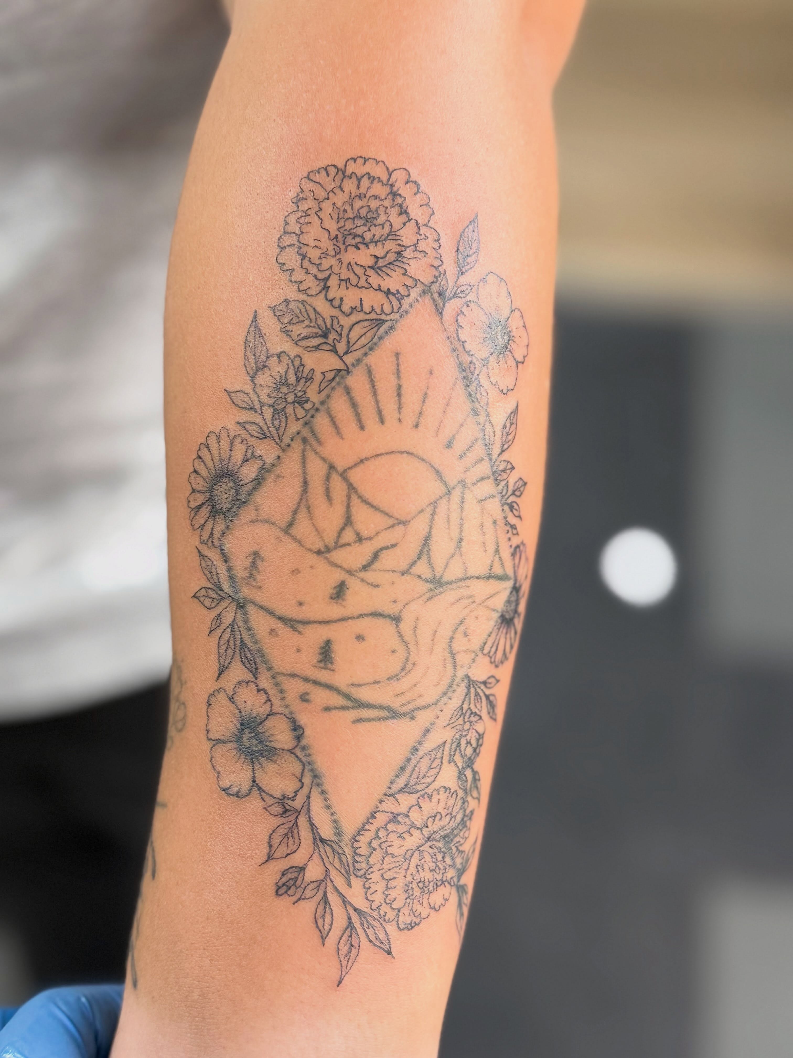 Flower and sunburst black and grey tattoo on the forearm by Tetiana