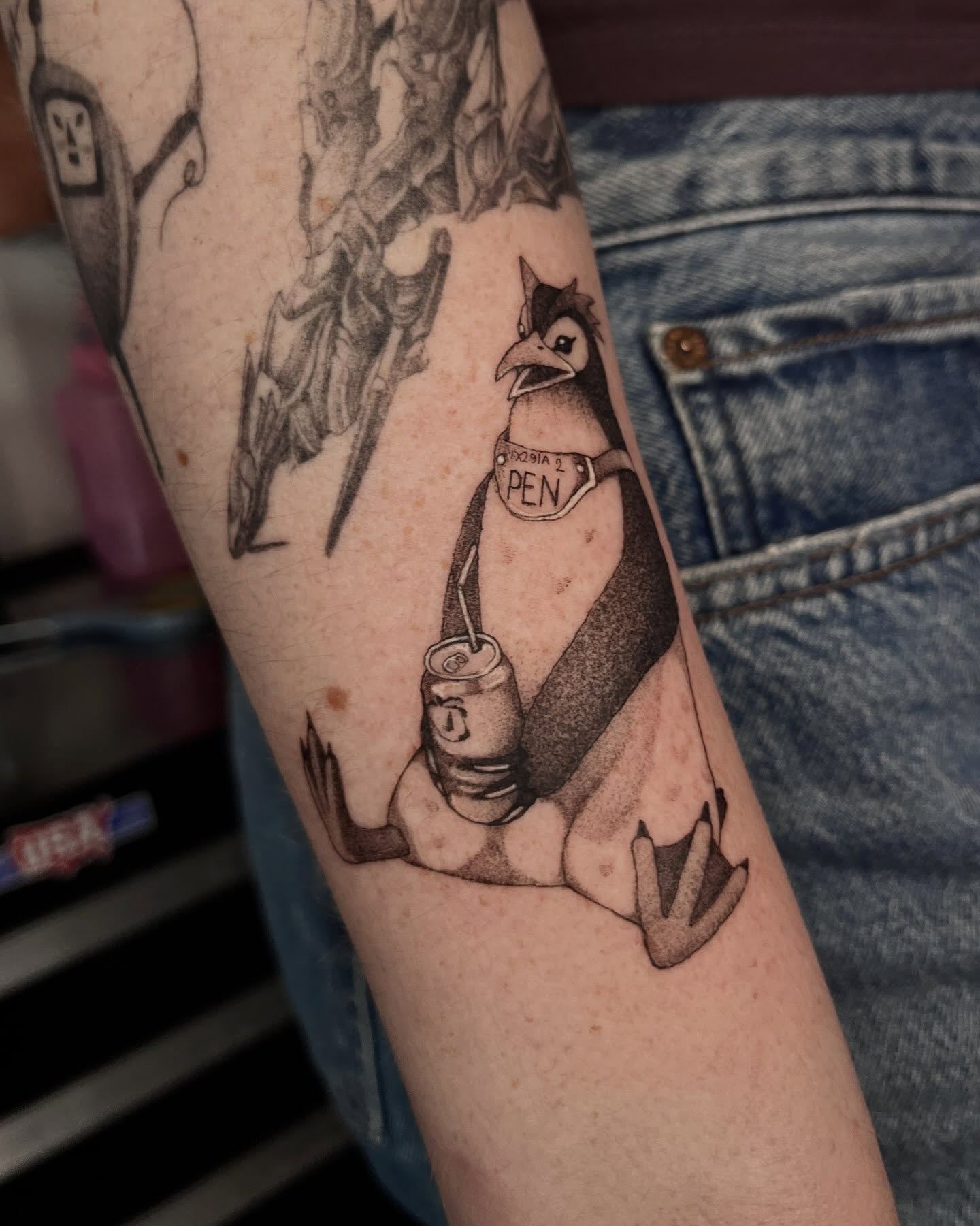 Penguin with can black and grey tattoo on the forearm by Sarah Jurgielewicz