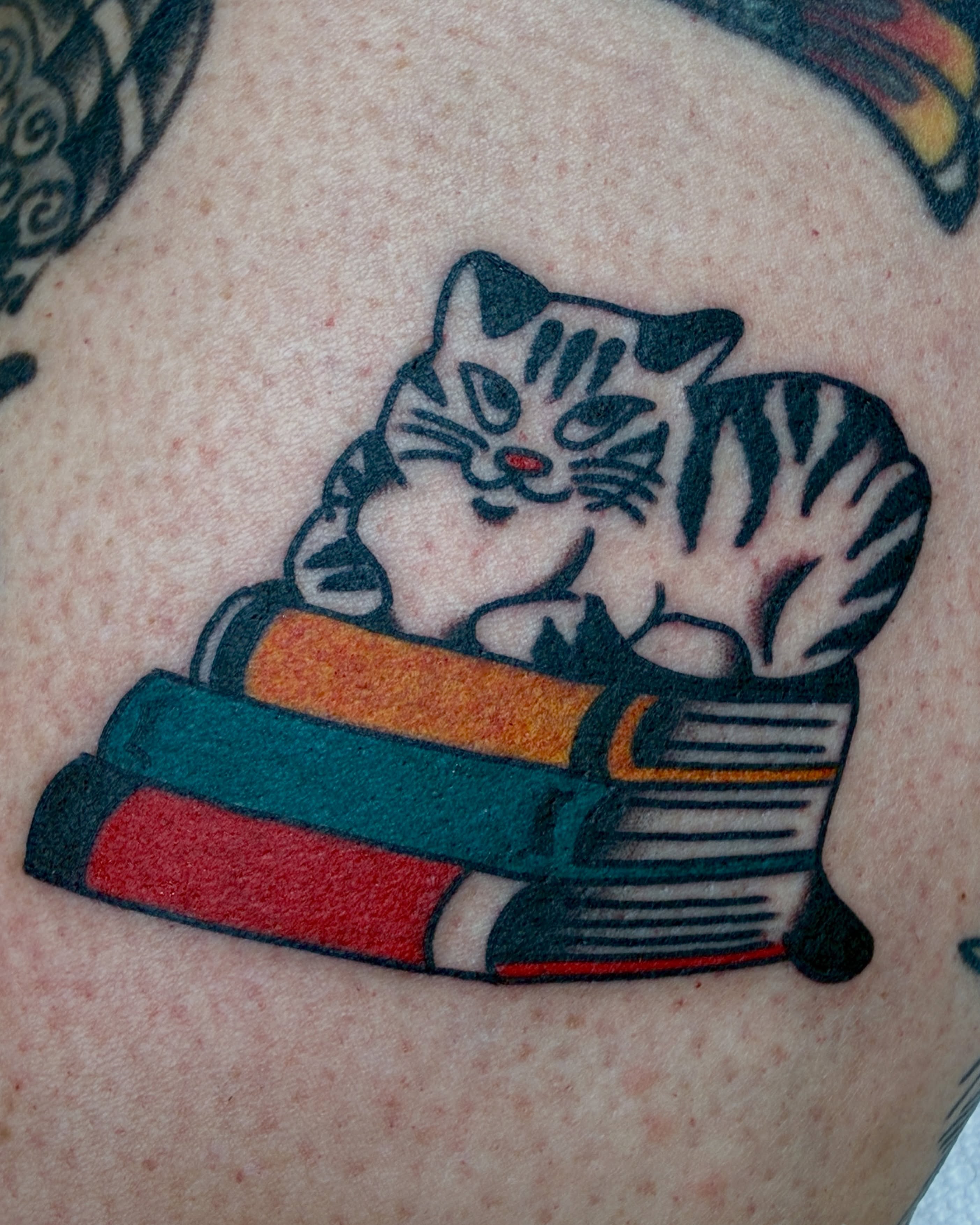 Cat and books American traditional tattoo on the shoulder by Sav Robinson