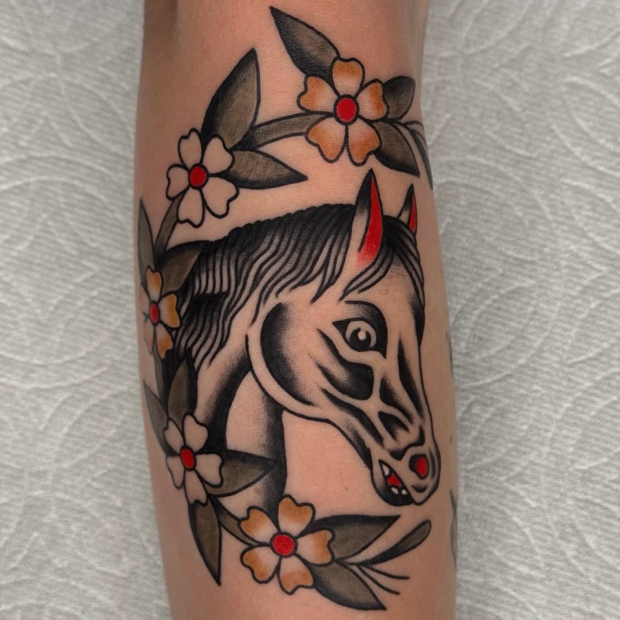 Horse head with floral wreath American traditional tattoo on the forearm by Bridgette Carberry