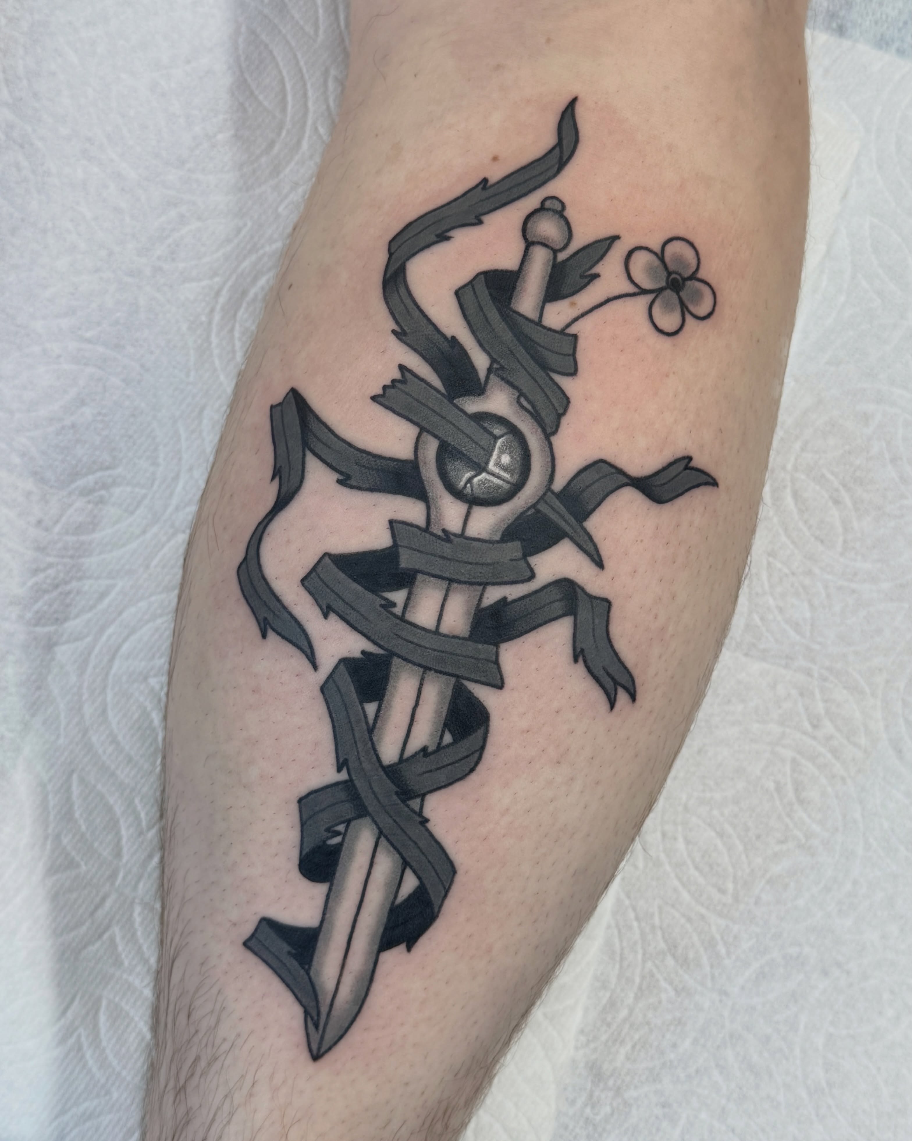 Sword and ribbon black and grey tattoo on the forearm by Nia (Knee-uhh) 🦷
