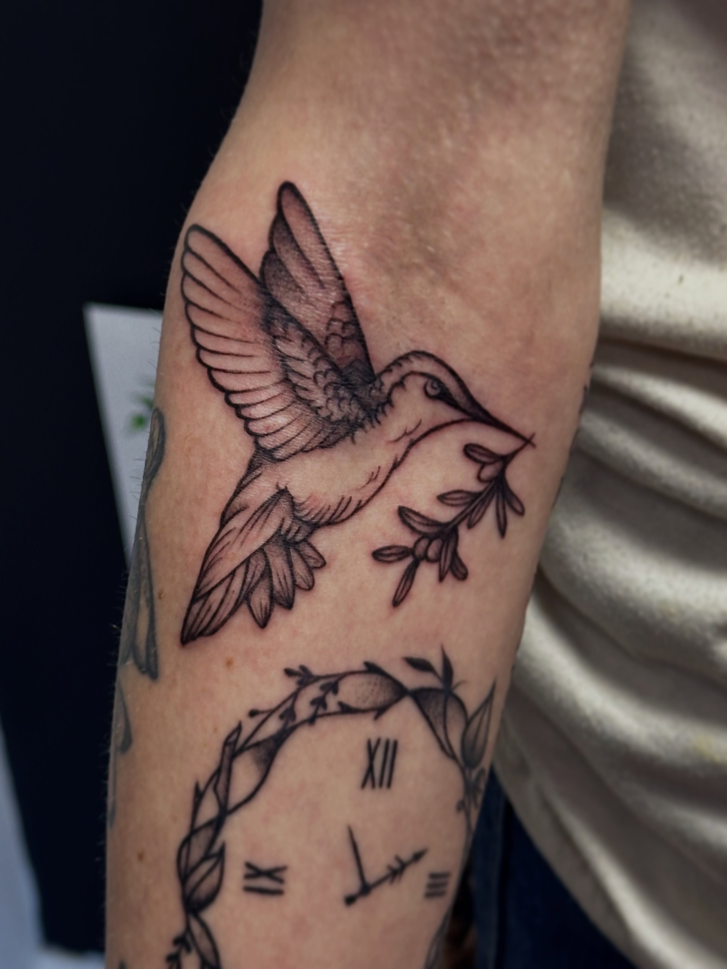 Hummingbird and clock black and grey tattoo on the forearm by Jocelyn