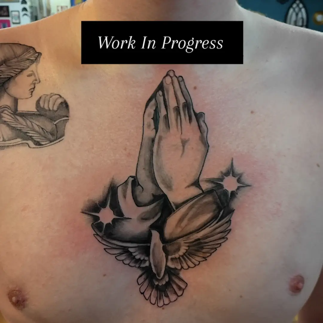 Praying hands with dove black and grey tattoo on the chest by Niki Jackson