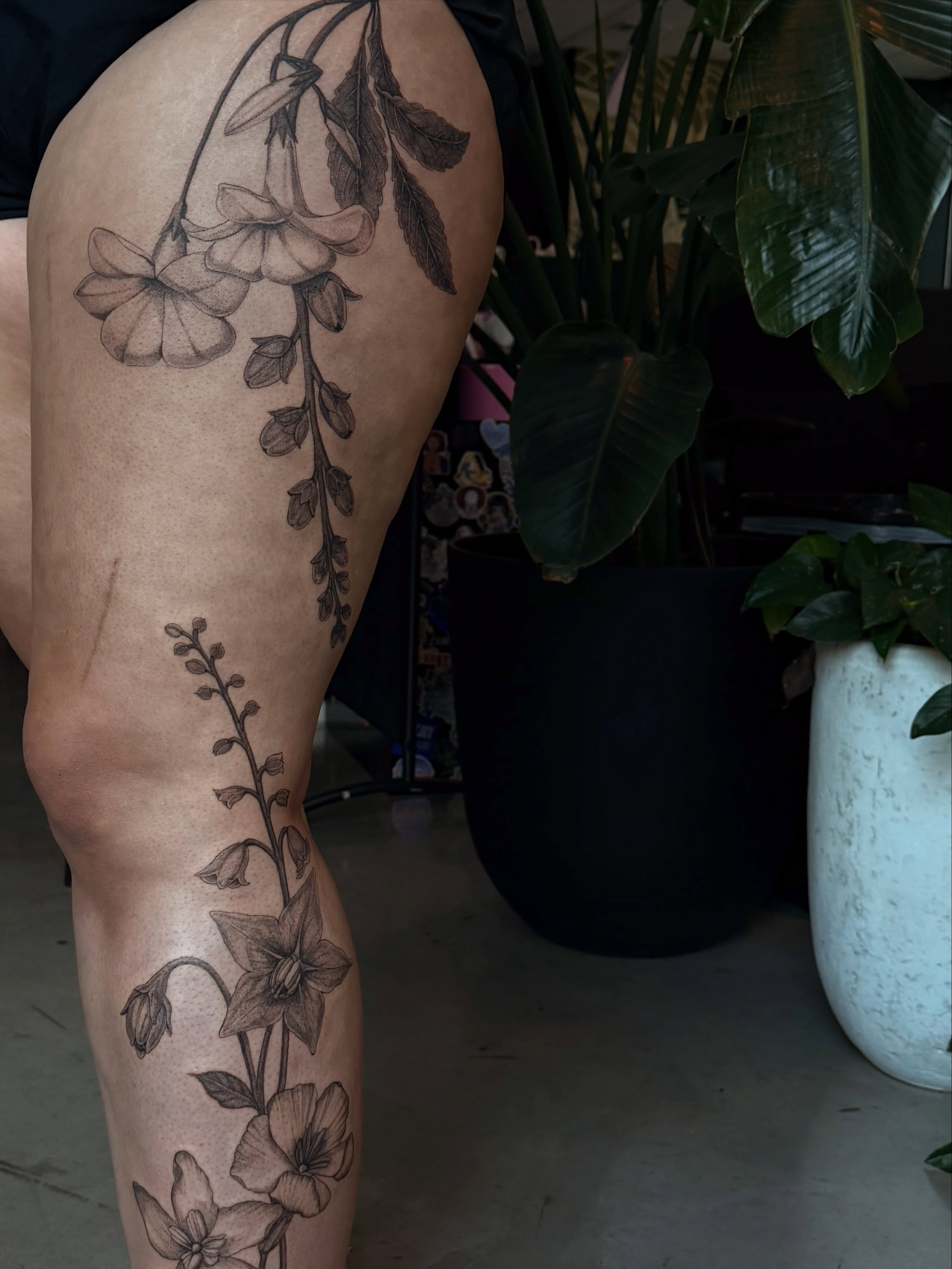 Flowers and vines black and grey tattoo on the thigh by Rachel