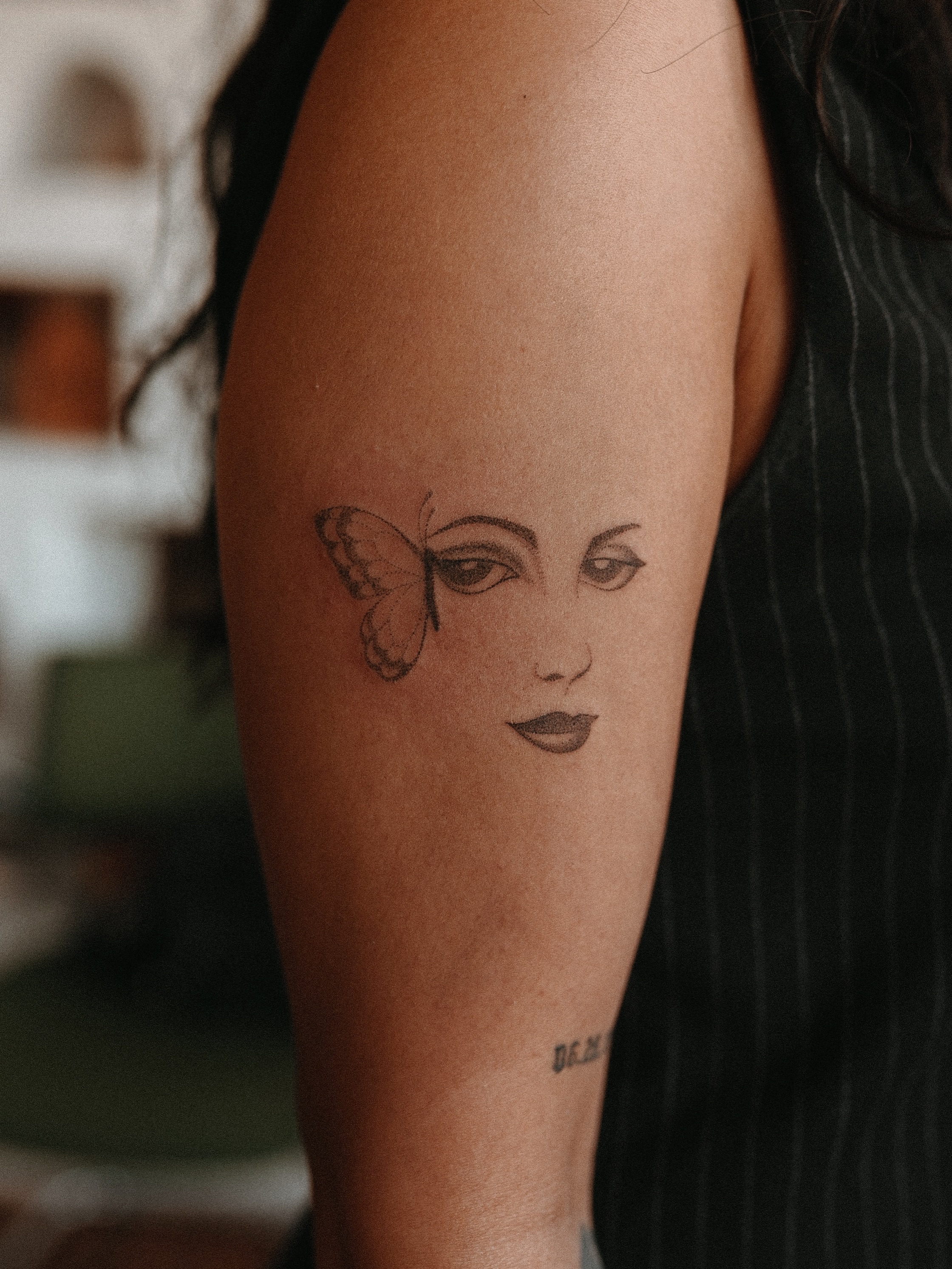 Woman's face with butterfly realism tattoo on the forearm by Grace Wise - Handpoke Tattoos