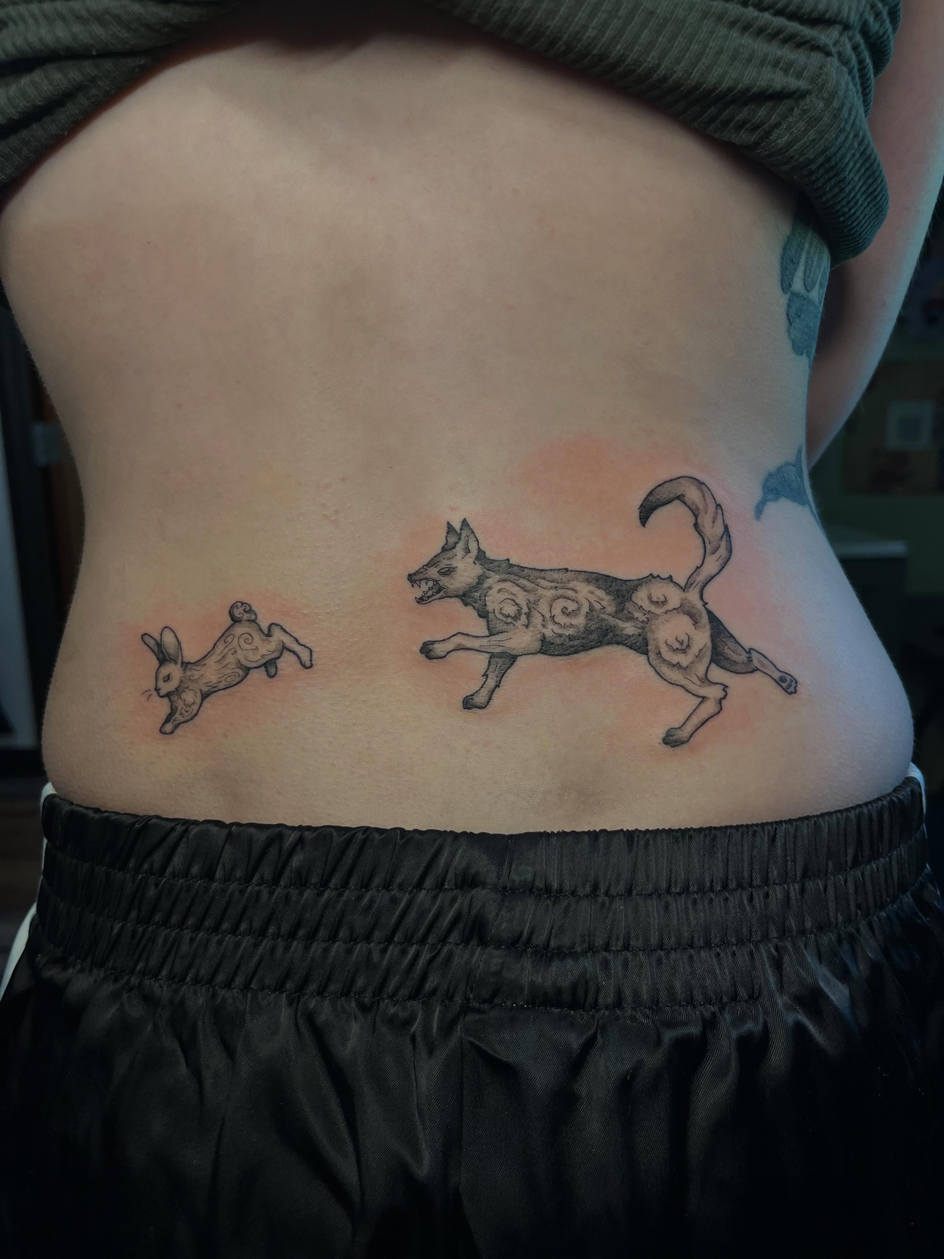 Dog chasing rabbit black and grey tattoo on the ribs by Jazzy