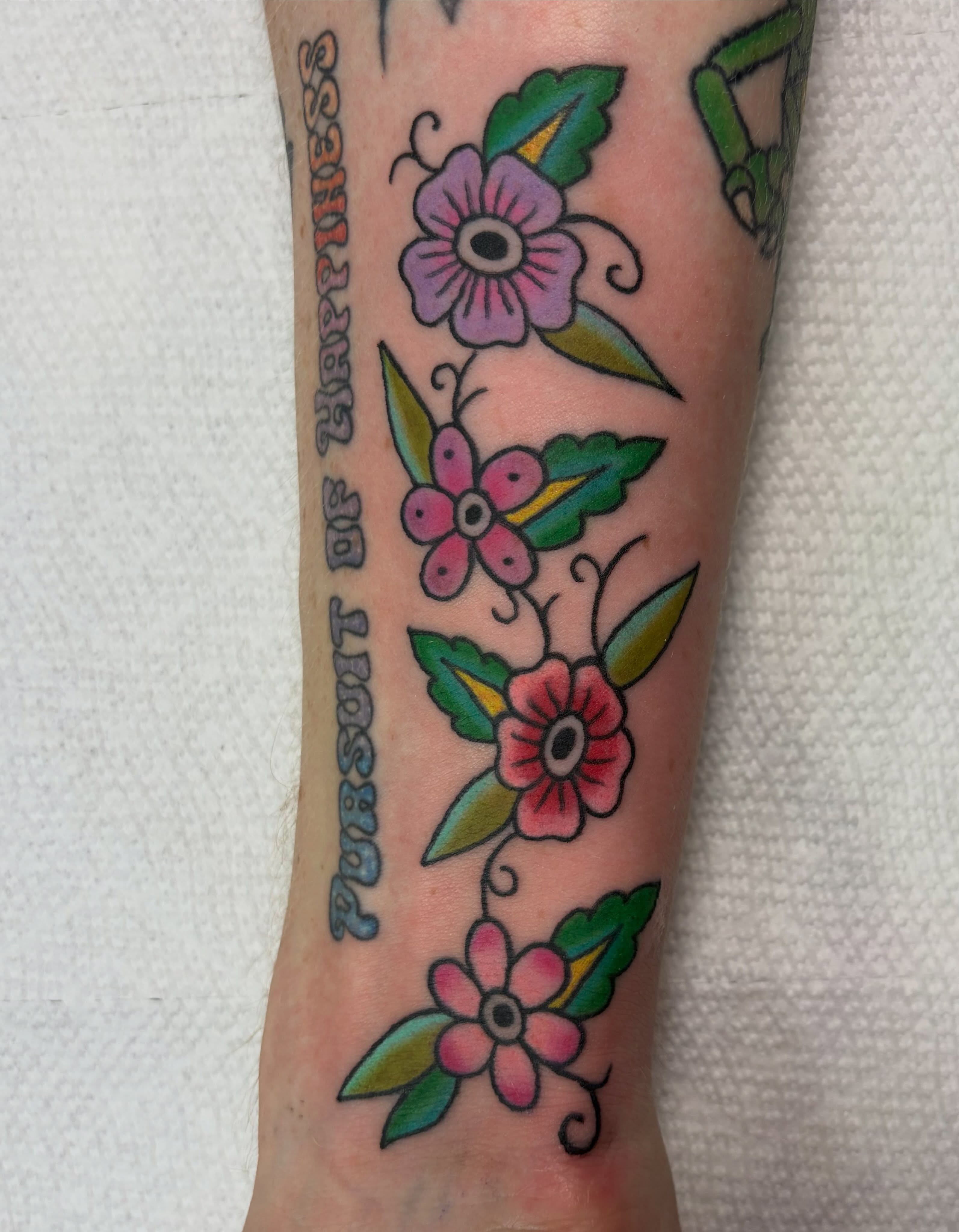 Flowers and text American traditional tattoo on the forearm by Juliet Miller