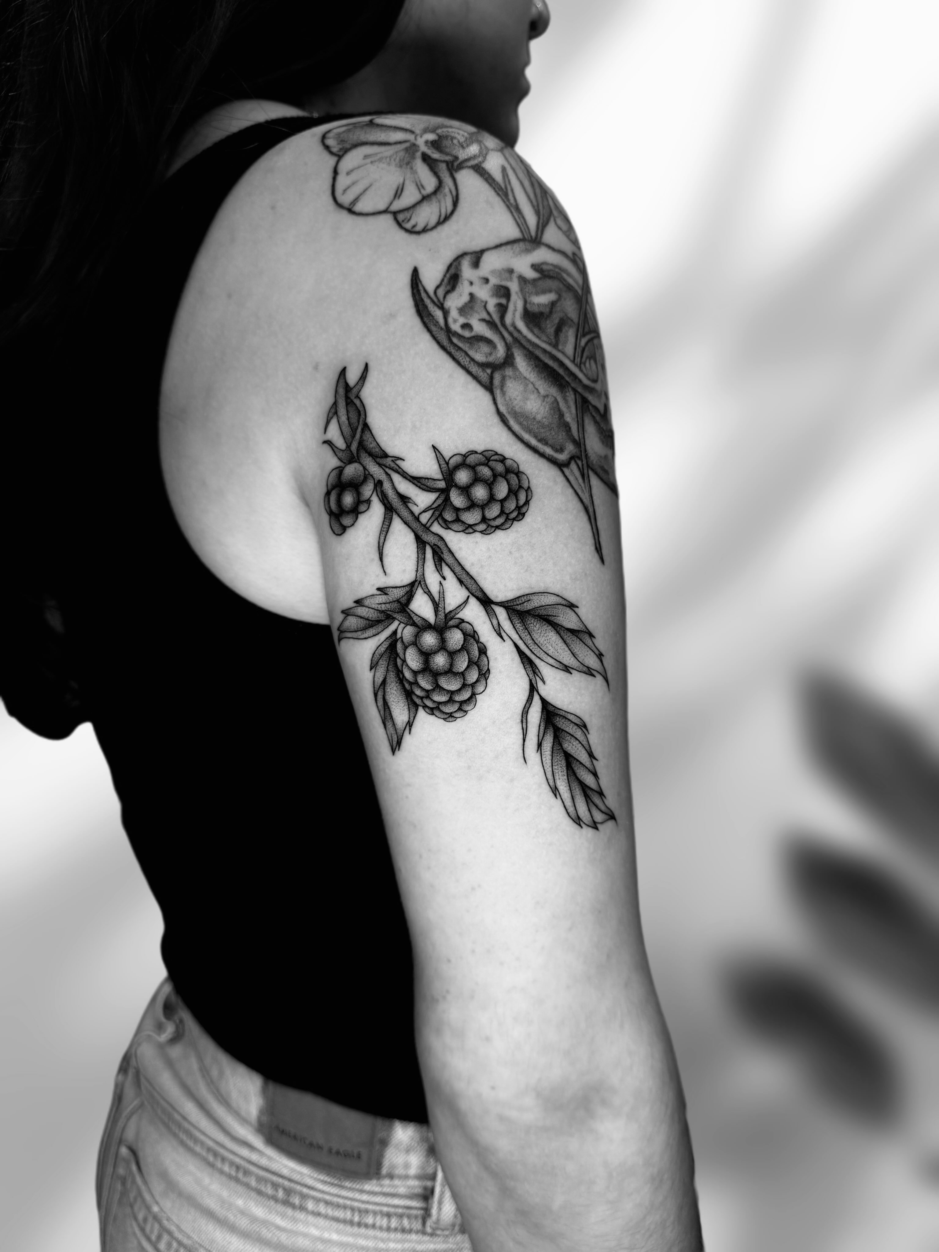 Berry branch with skull realism tattoo on the upper arm by Ingrid Rojas