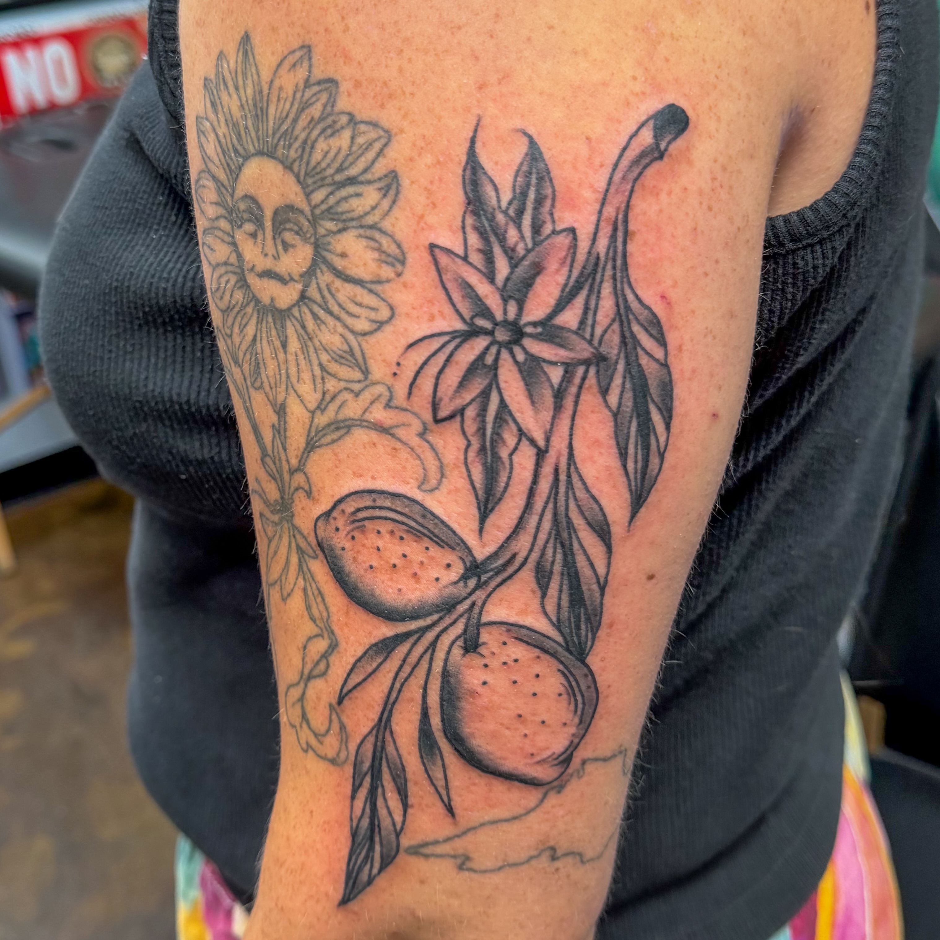 Sunflower and fruit black and grey tattoo on the forearm by Zac Tattooer