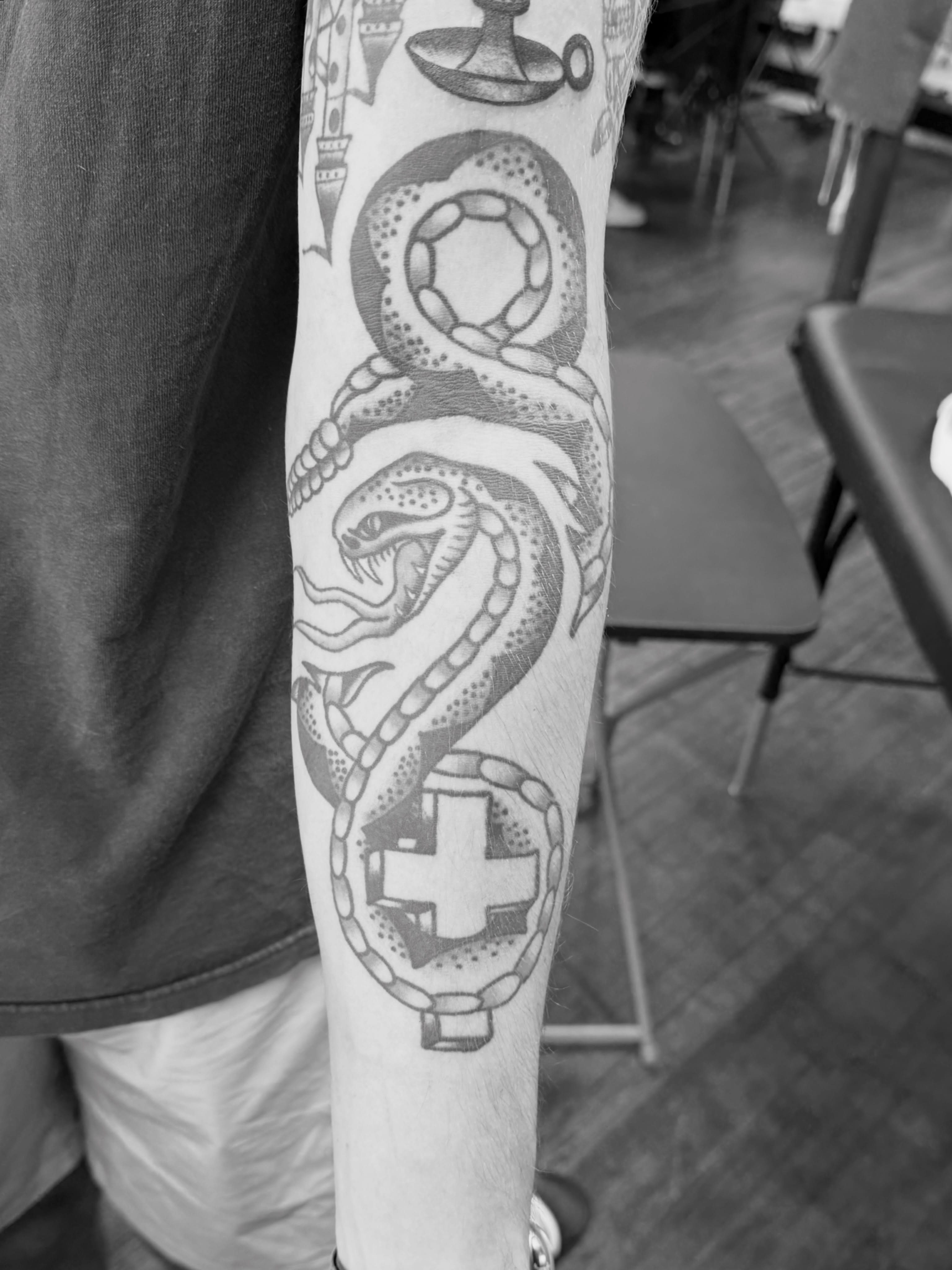 Snake and medical cross black and grey tattoo on the forearm by Aaron ulfstam