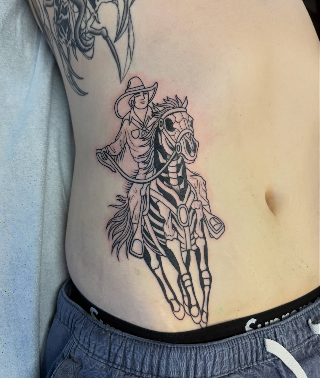 Cowboy riding horse black and grey tattoo on the ribs by Connie Fiorino - Tattoo Artist