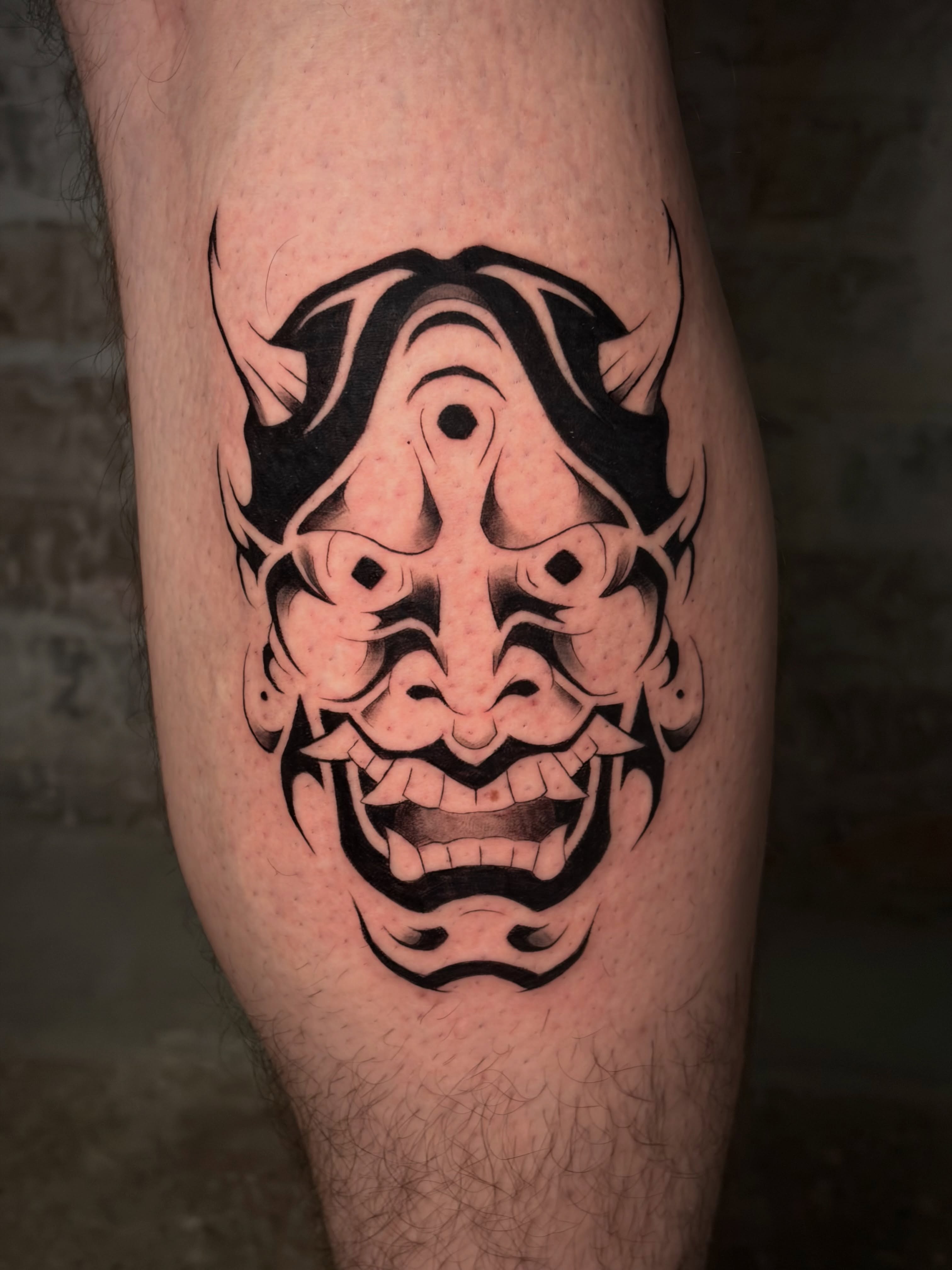 Demon mask black and grey tattoo on the thigh by Musa Selman