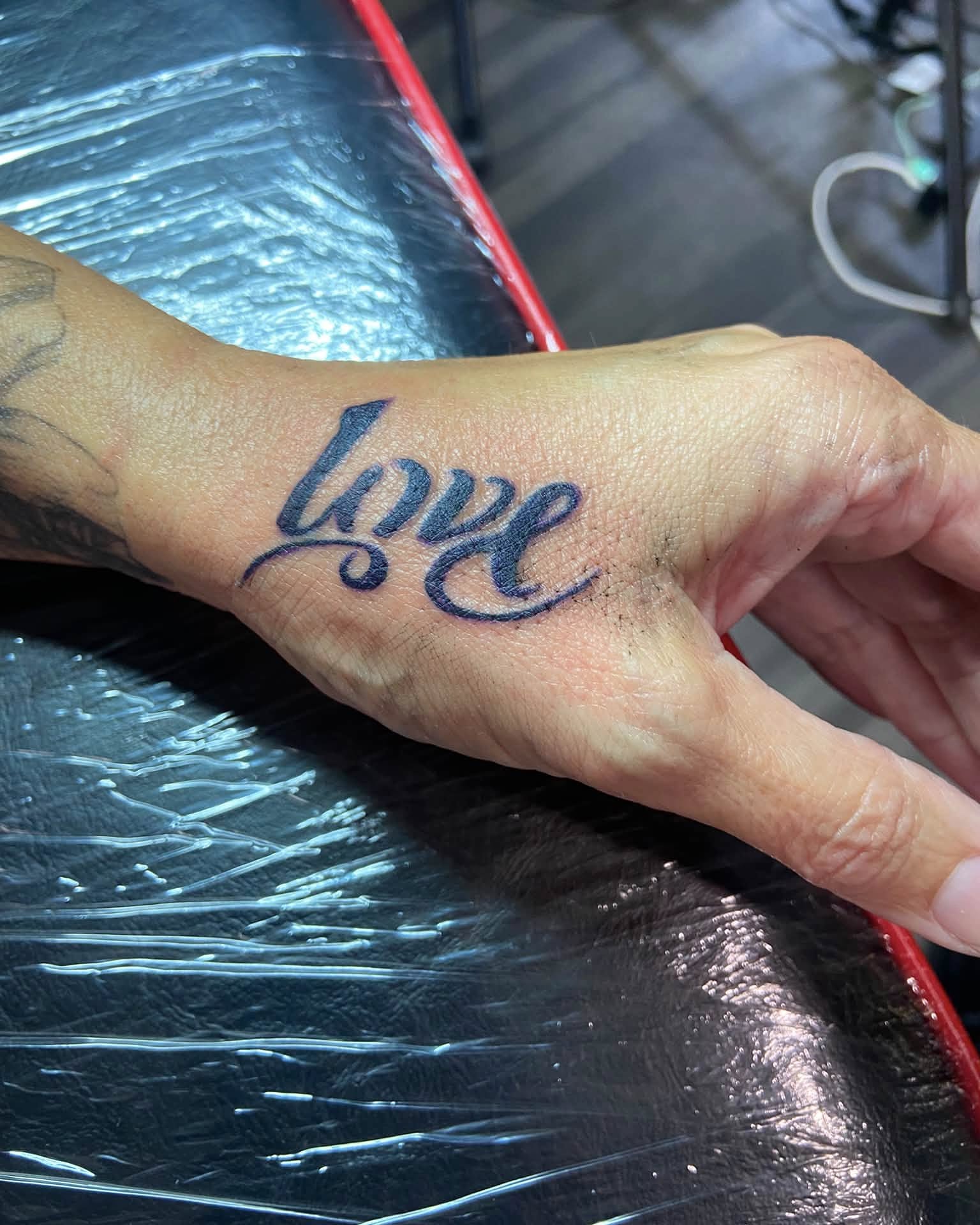 Love lettering script tattoo on the hand by Mike Berry